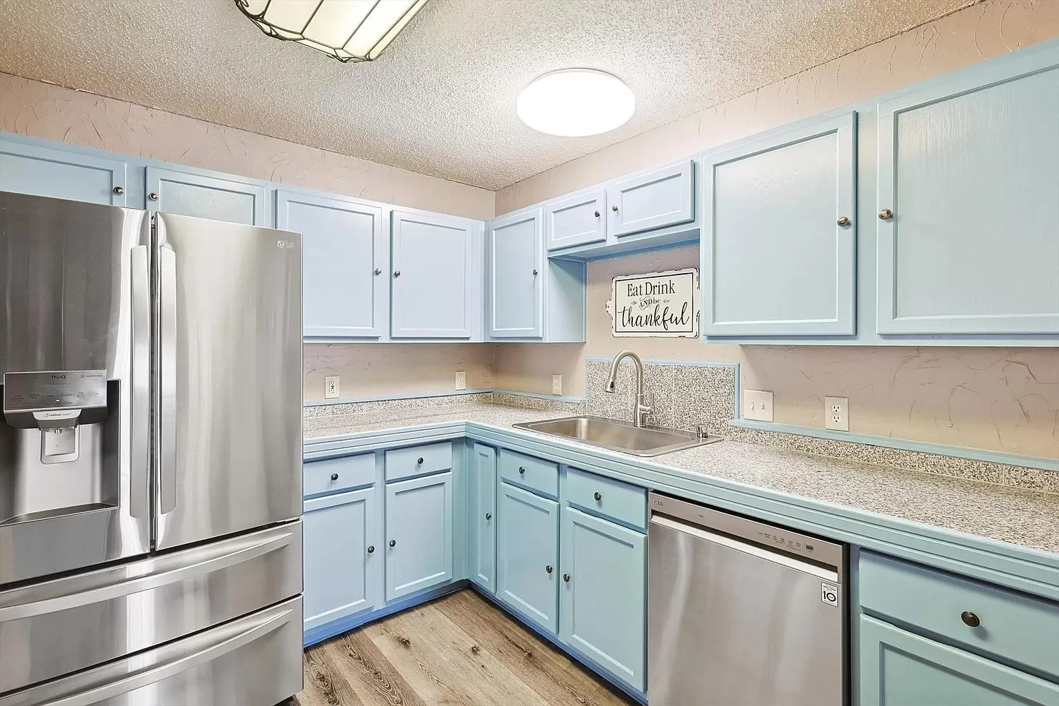 Kitchen featuring light blue cabinetry, granite-style countertops, stainless steel appliances, and wood-finish flooring