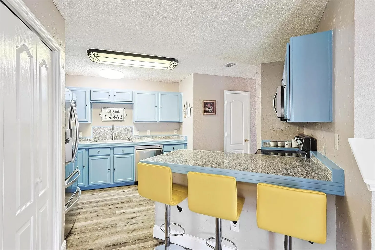 Kitchen featuring custom blue cabinetry, stainless steel appliances, and a breakfast bar with a granite-style countertop