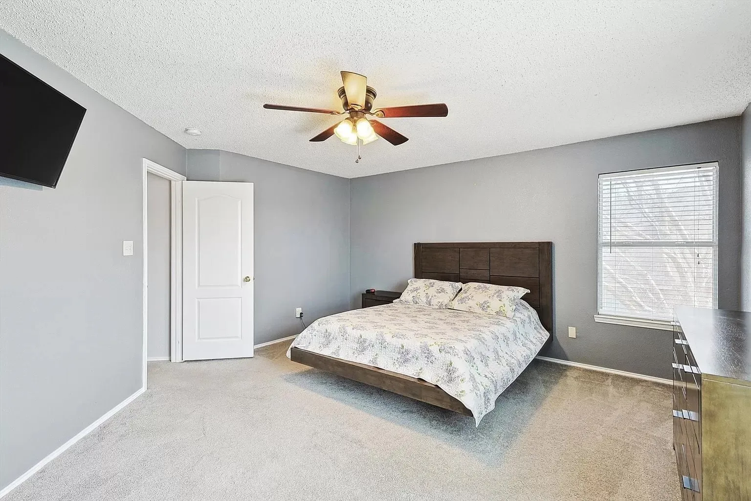 Carpeted interior space featuring a ceiling fan with integrated lighting, a window with horizontal blinds, and a white paneled door