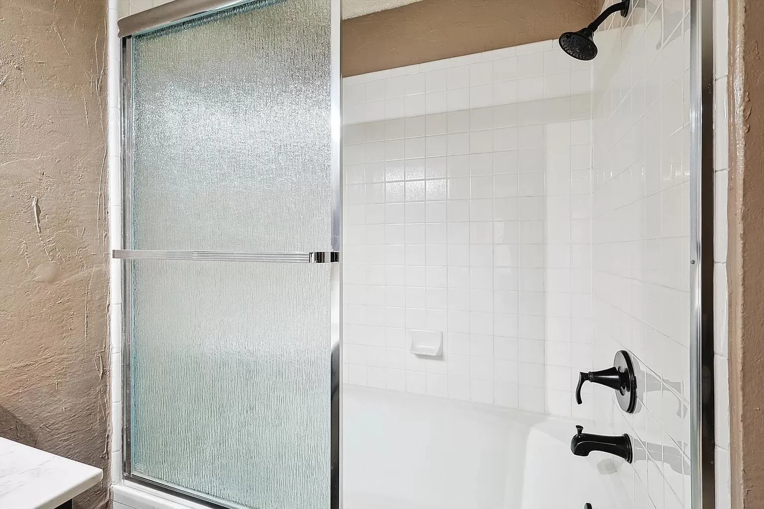 White subway tile shower surround with a matte black showerhead and fixtures, complemented by a textured glass sliding shower door