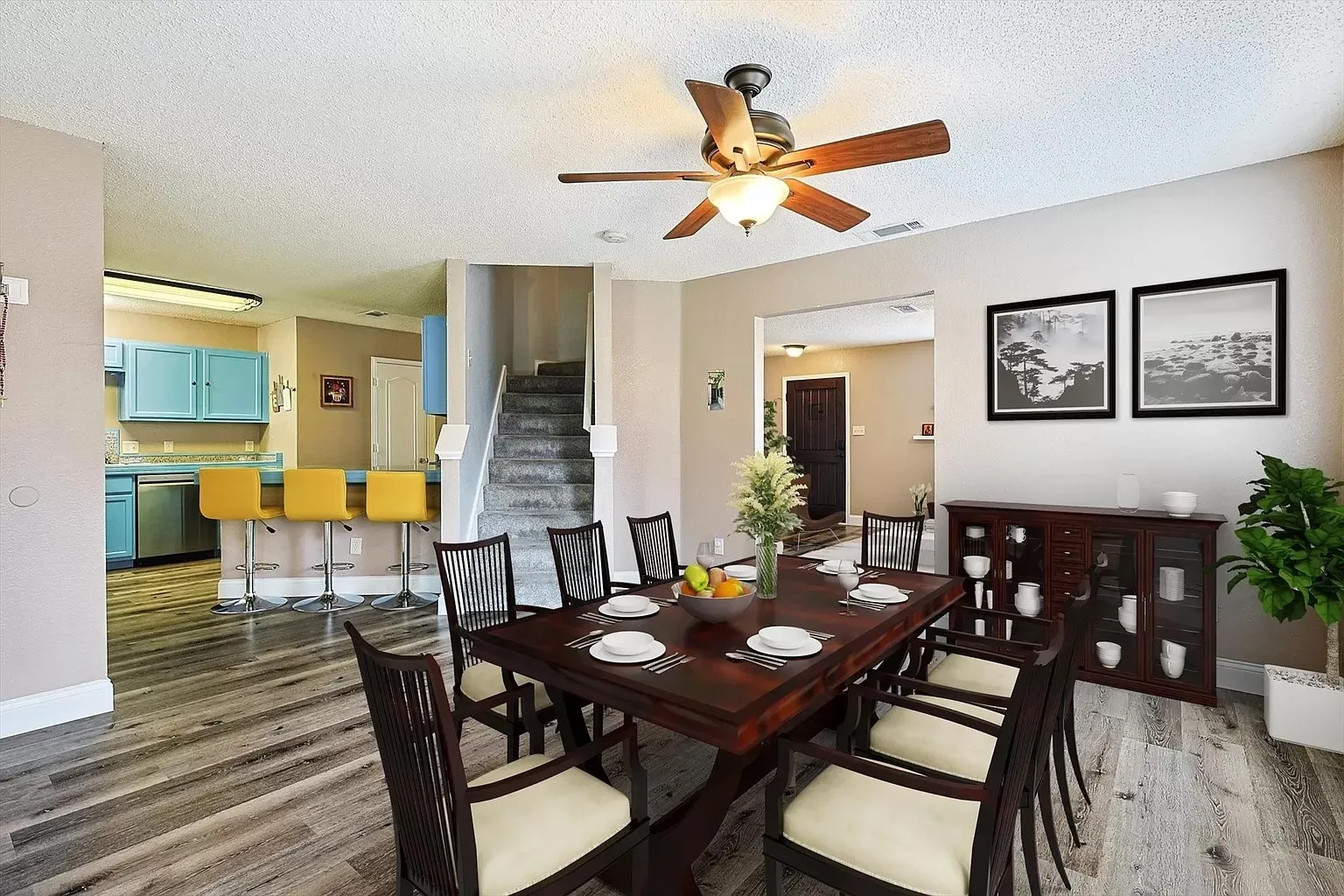 Open-concept dining area featuring wood-finish flooring, a ceiling fan, and a pass-through counter to the kitchen with light blue cabinetry and stainless steel appliances