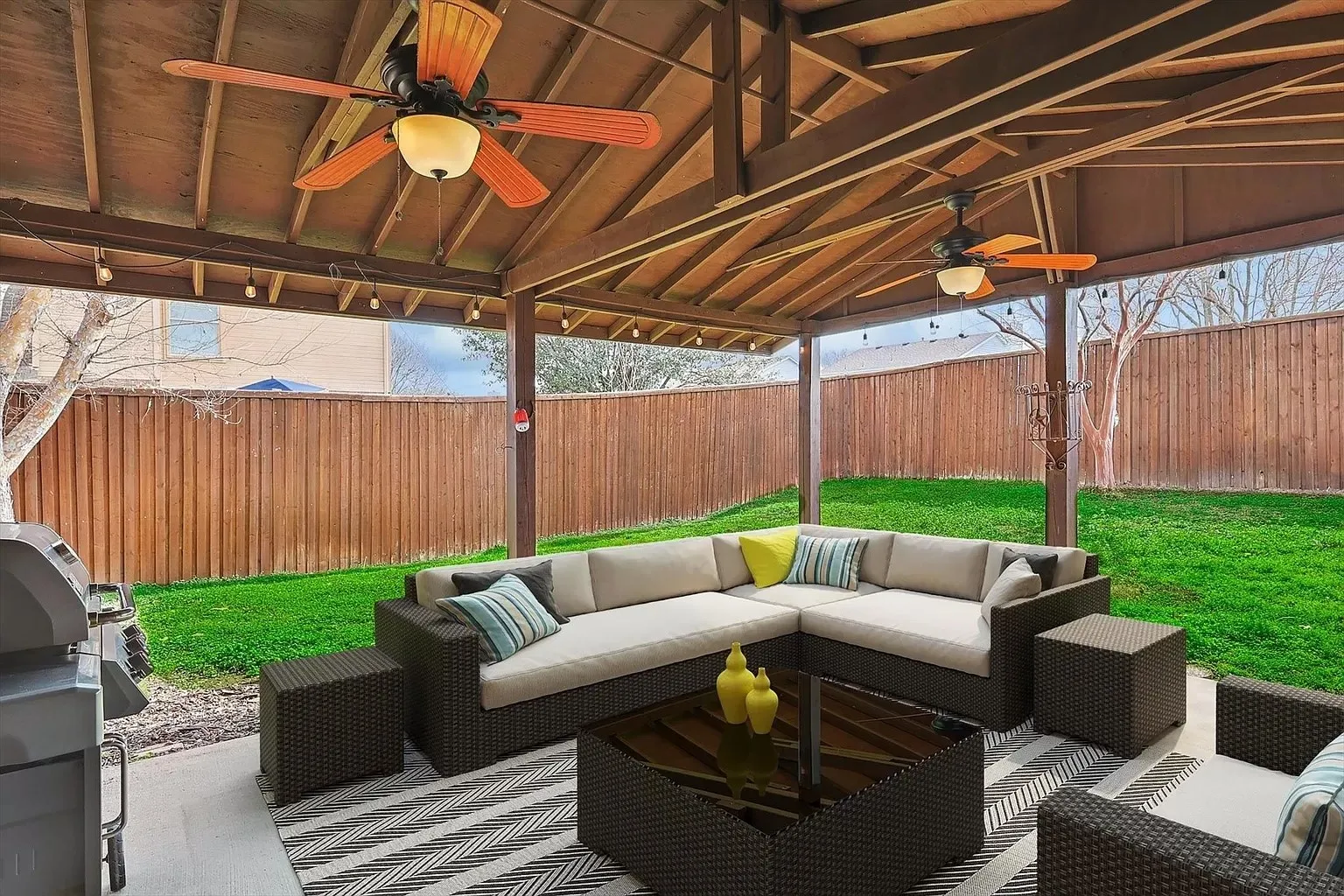 Covered patio with exposed wood beam ceiling, two ceiling fans with lighting, and string lighting