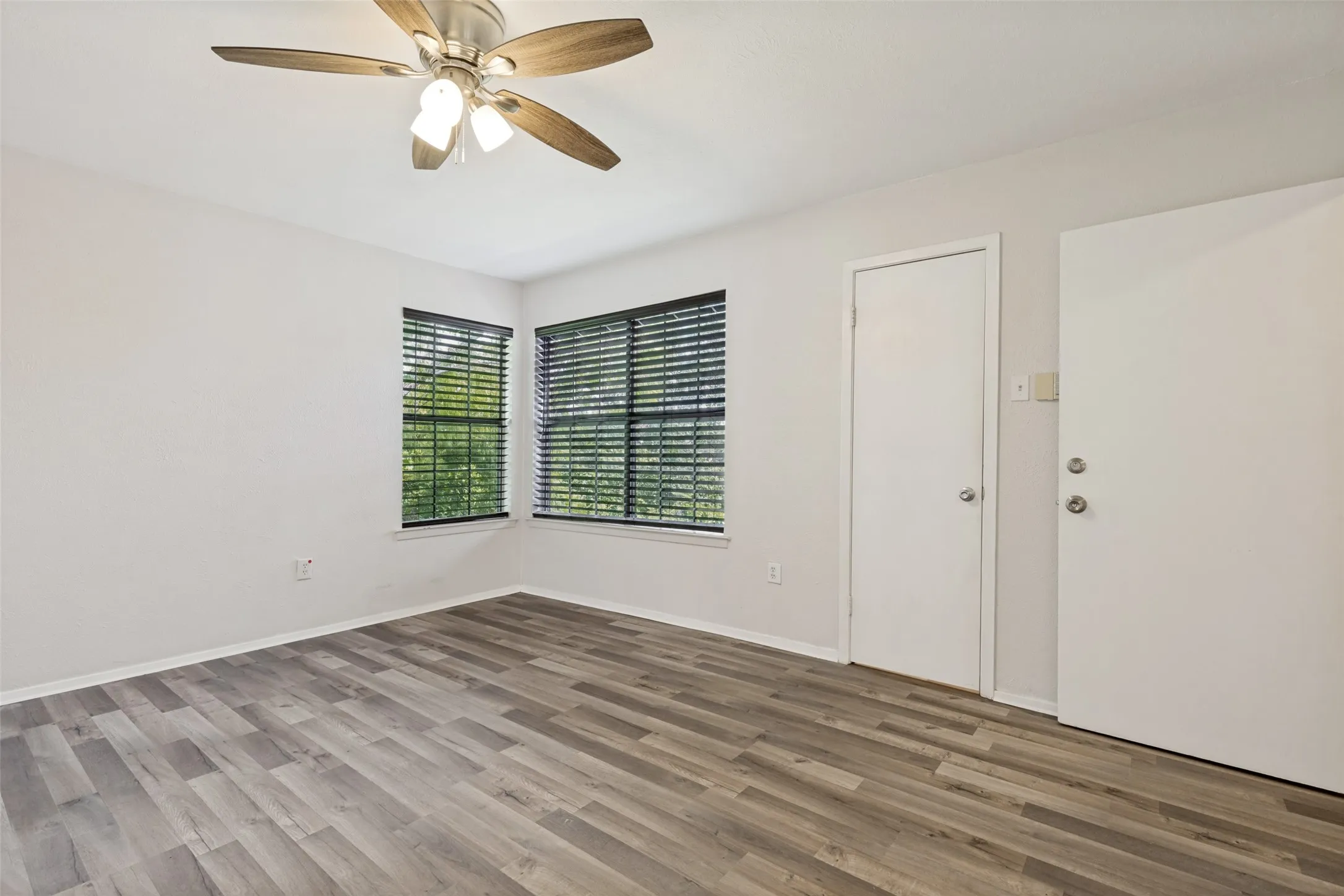 Spacious interior with wood-finish flooring, light neutral wall tones, and corner windows featuring blinds
