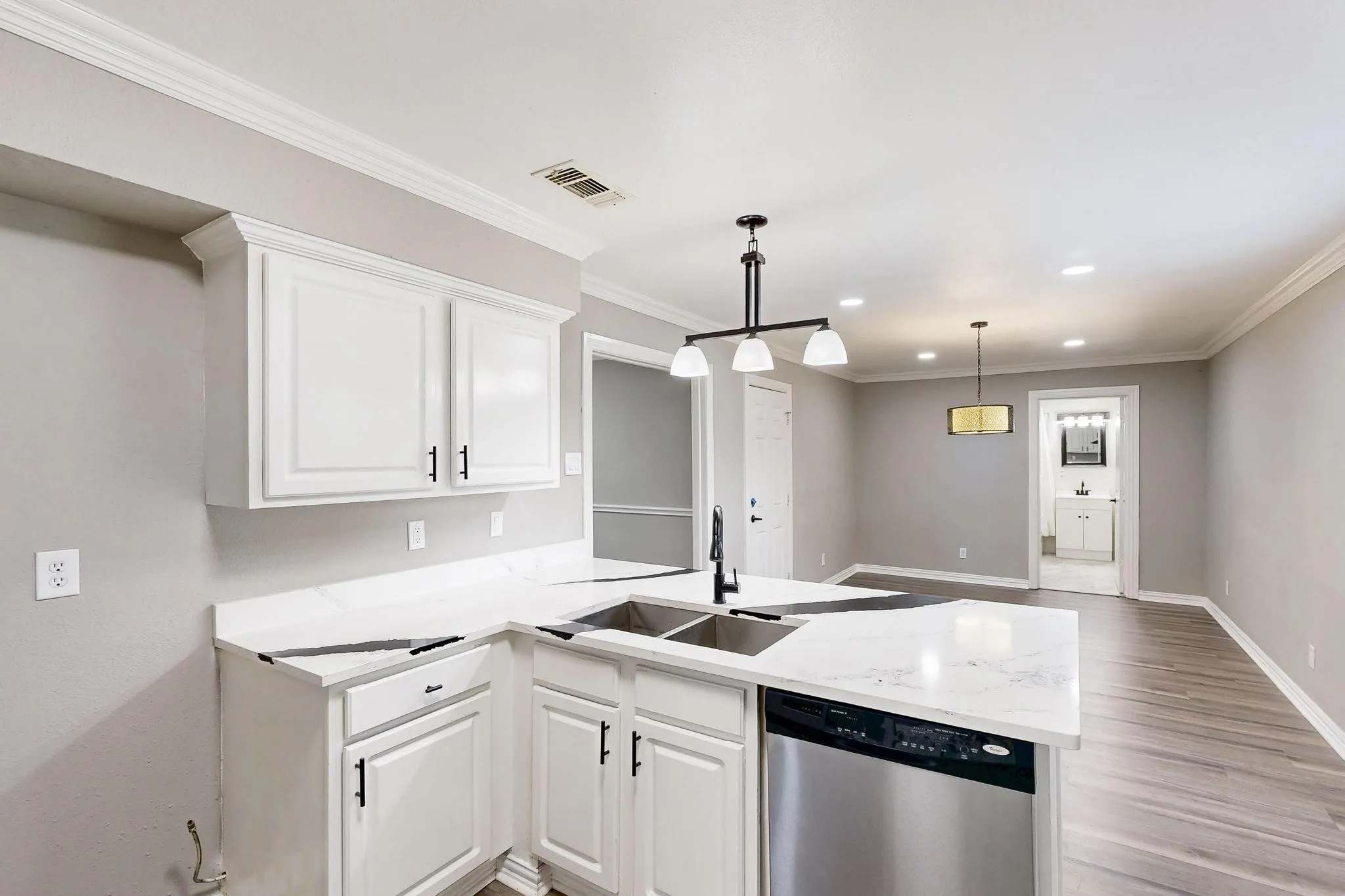 Kitchen featuring stainless steel dishwasher, a sink, a peninsula, baseboards, and white cabinets
