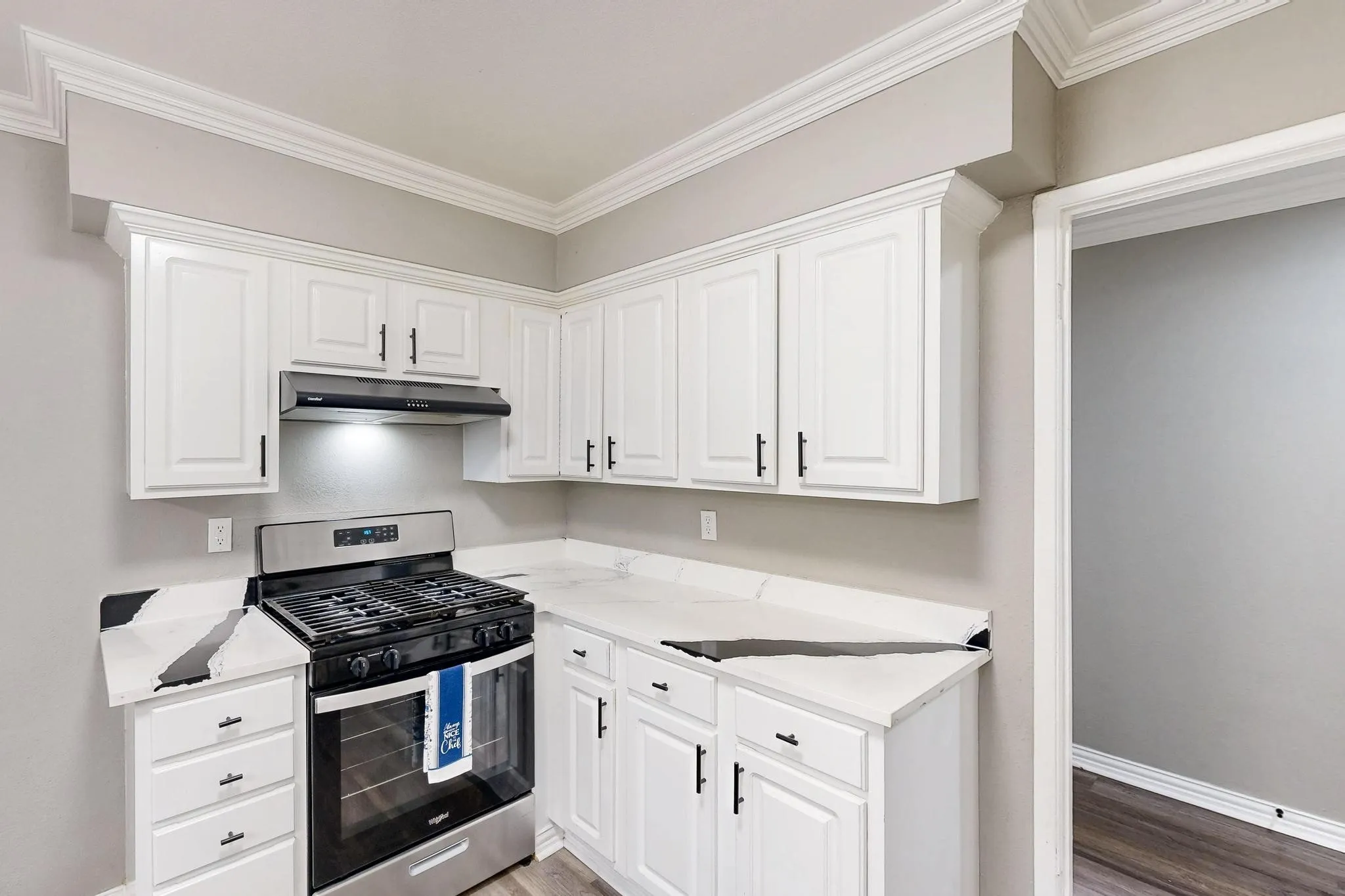 Kitchen with stainless steel gas range, under cabinet range hood, white cabinetry, and ornamental molding