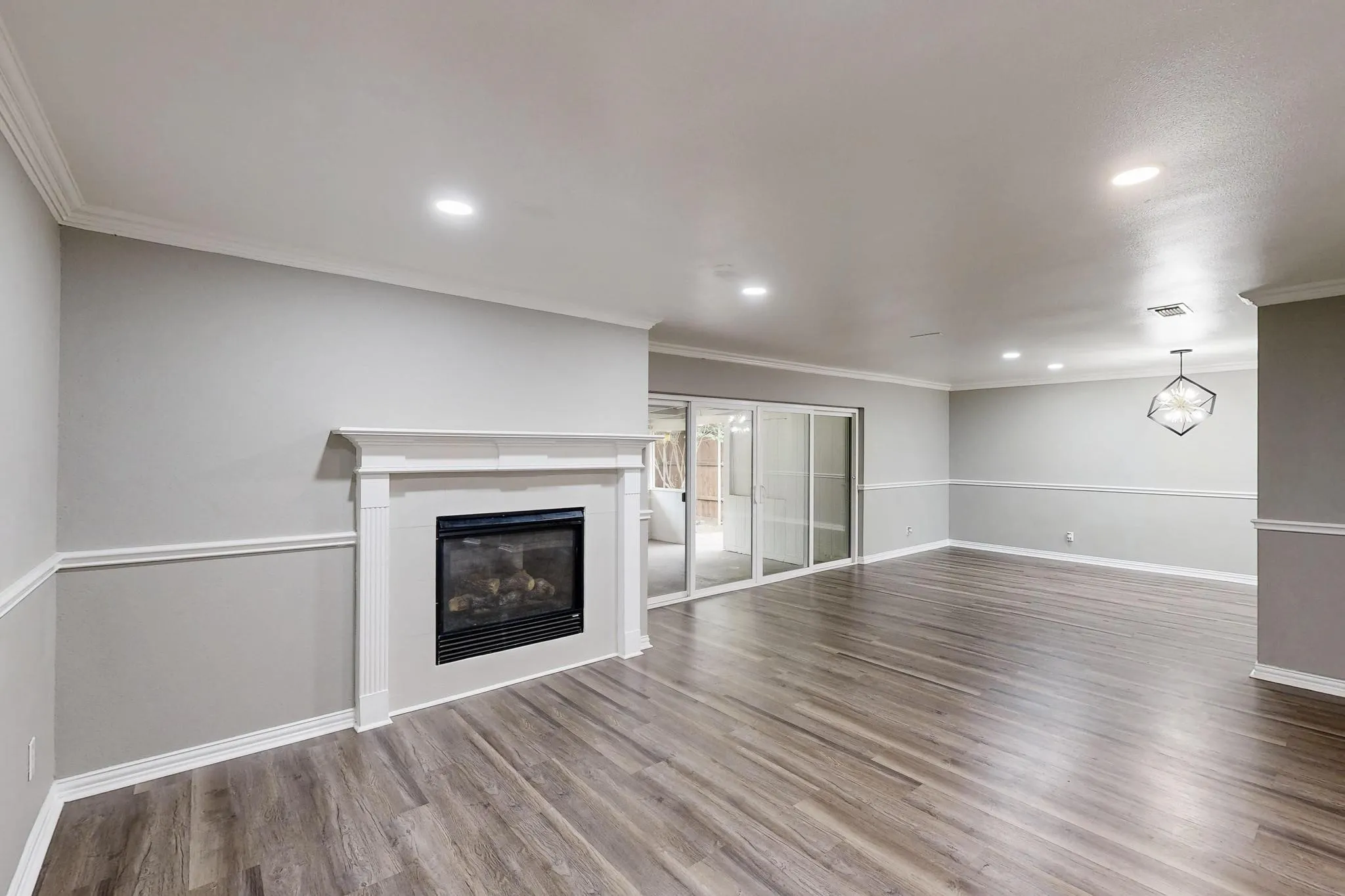 Unfurnished living room featuring wood finished floors, a glass covered fireplace, ornamental molding, baseboards, and recessed lighting