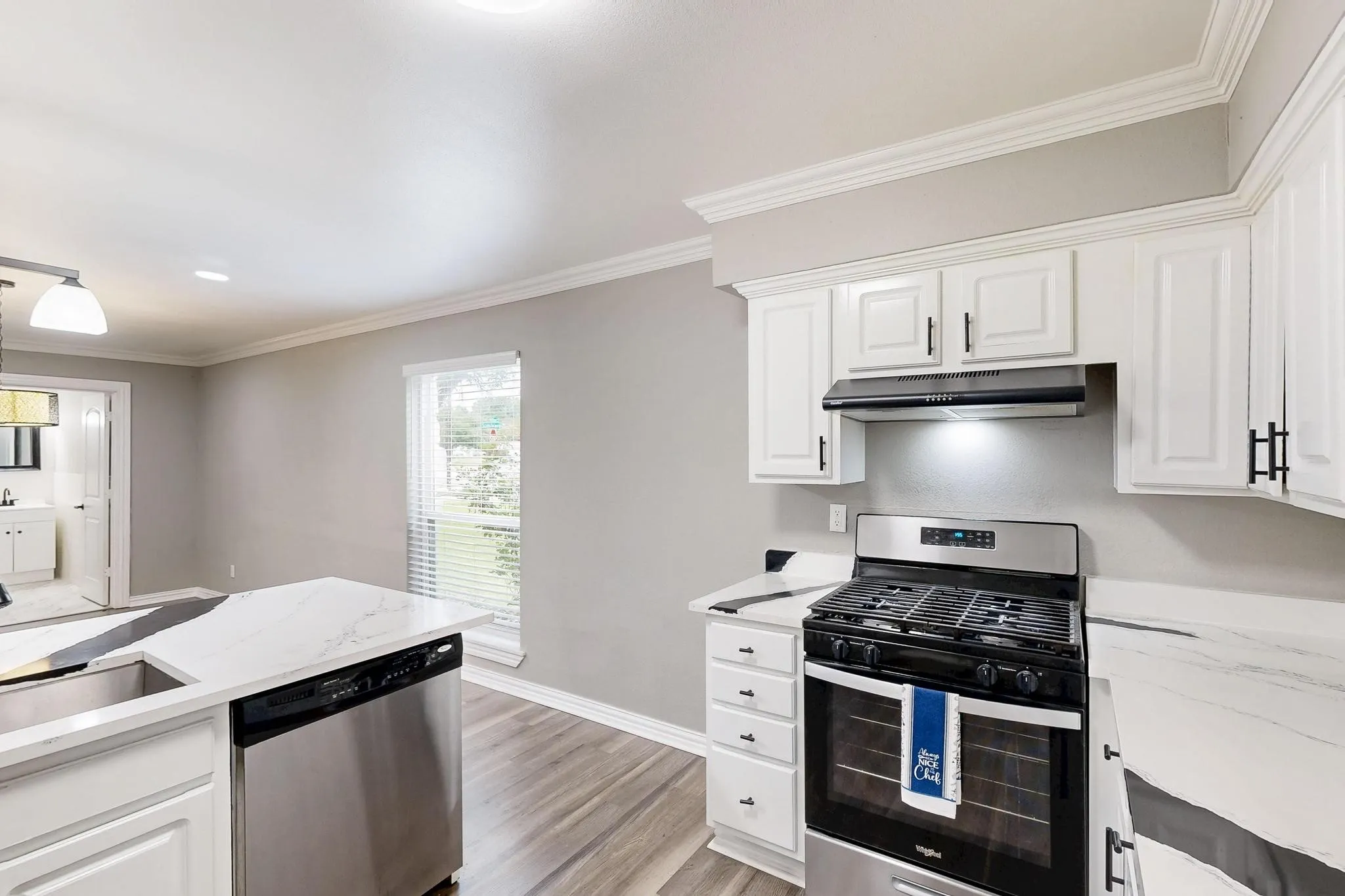 Kitchen featuring stainless steel appliances, under cabinet range hood, white cabinetry, crown molding, and light wood finished floors
