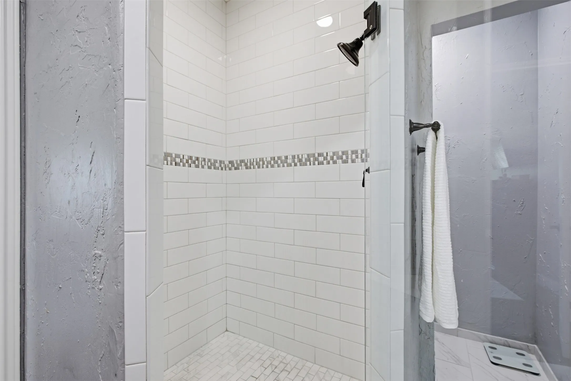 Walk-in shower with white subway tile, mosaic accent band, oil-rubbed bronze fixtures, and glass enclosure