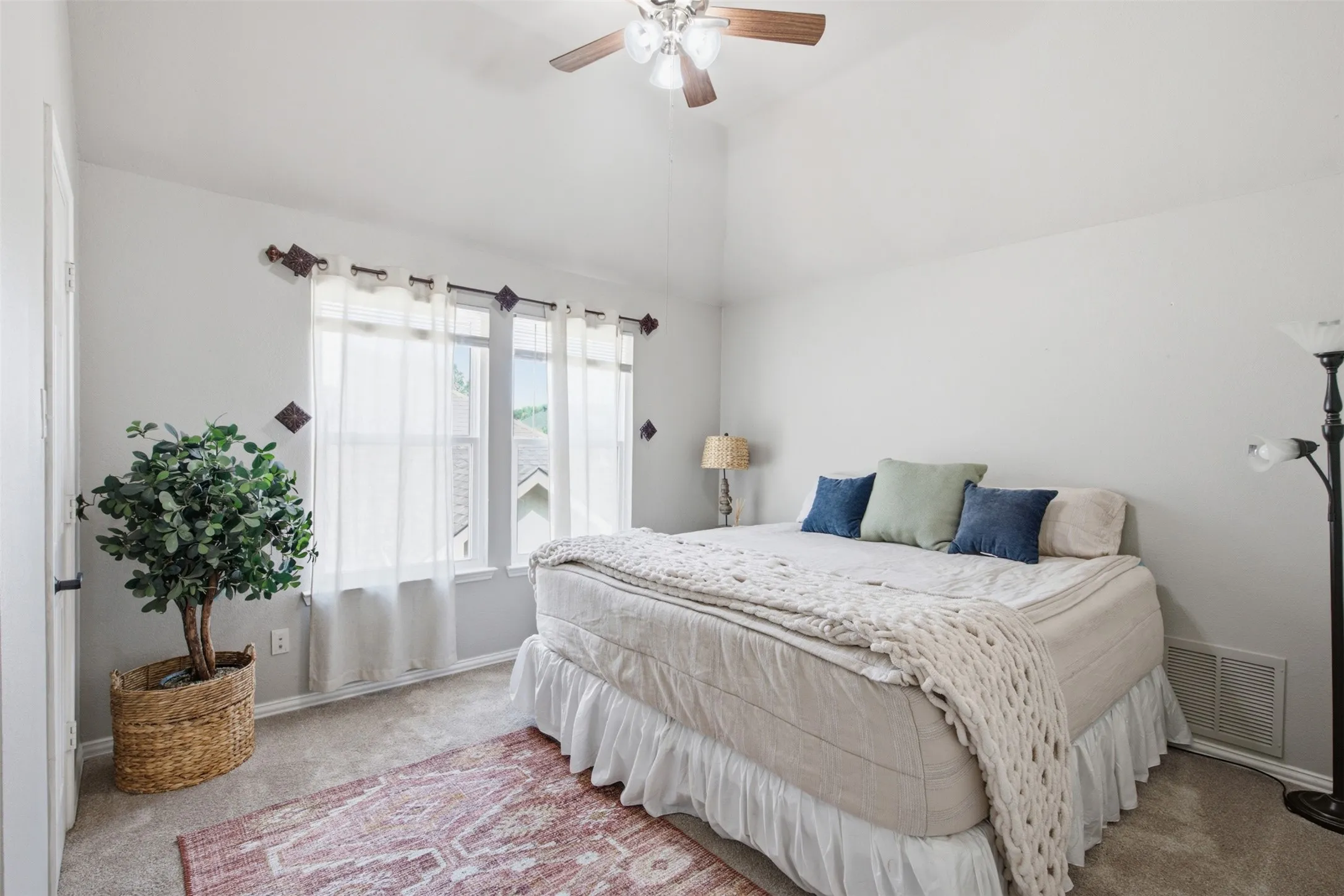 Vaulted ceiling bedroom featuring carpet flooring, a multi-pane window with sheer curtains, and a ceiling fan with light fixture