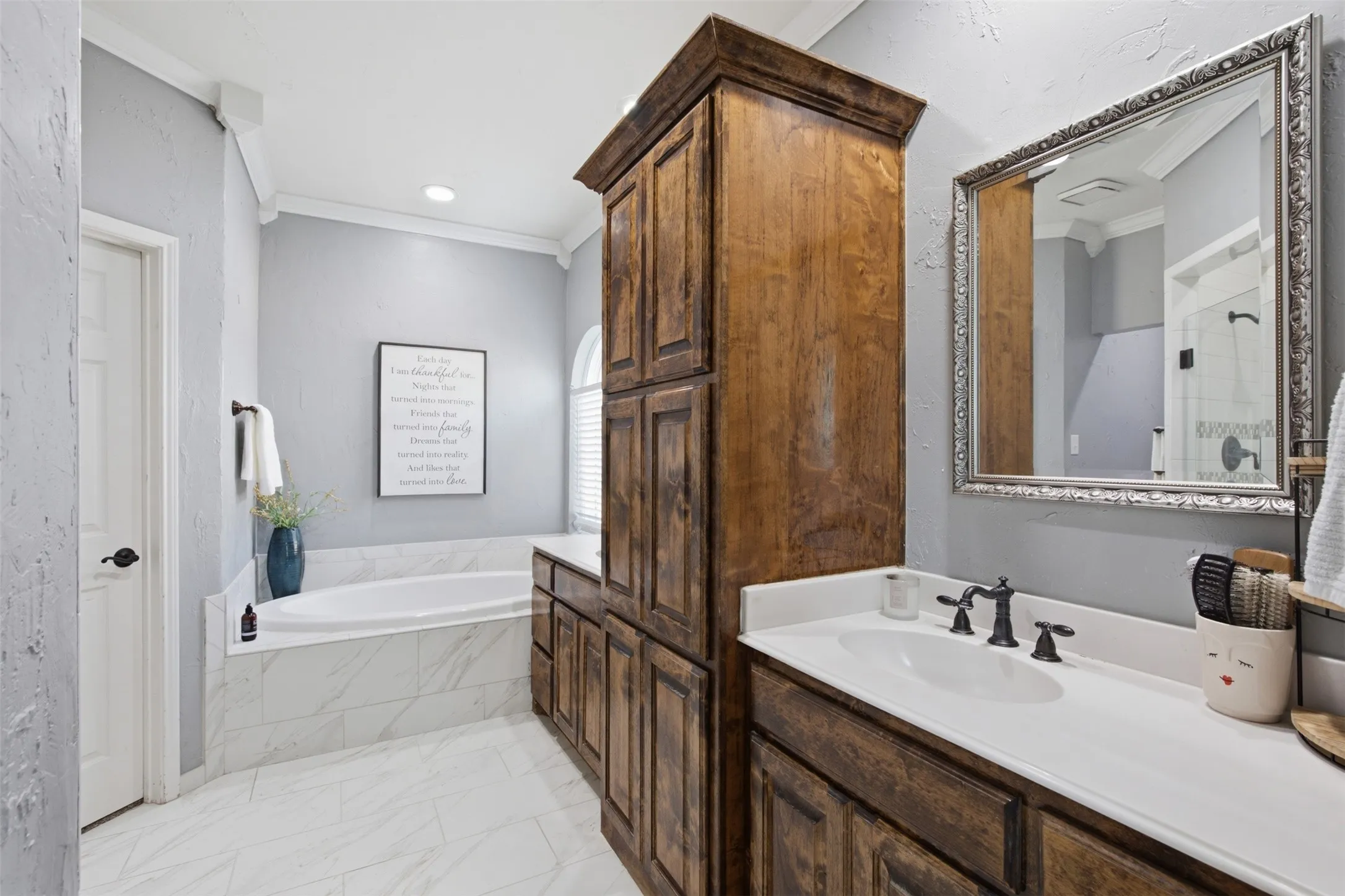 Bathroom featuring a soaking tub with a tiled surround, wood-finish cabinetry, a single vanity with a white countertop, and an ornate framed mirror