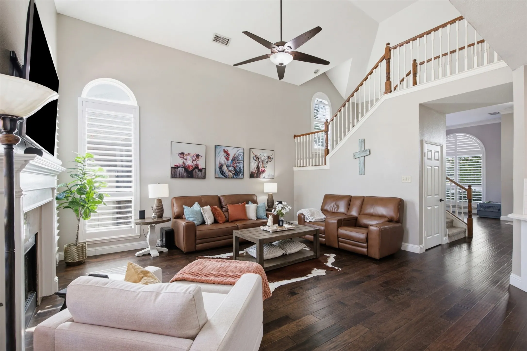 Vaulted living area featuring wood-finish flooring, a white mantelpiece, arched windows with shutters, and an upper-level staircase with white balusters and wood handrails