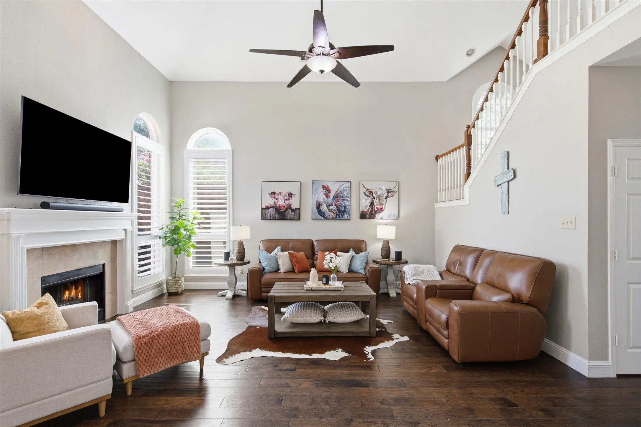 Spacious living area featuring high vaulted ceilings, rich wood-finish flooring, and a fireplace with a stone surround and a white mantel
