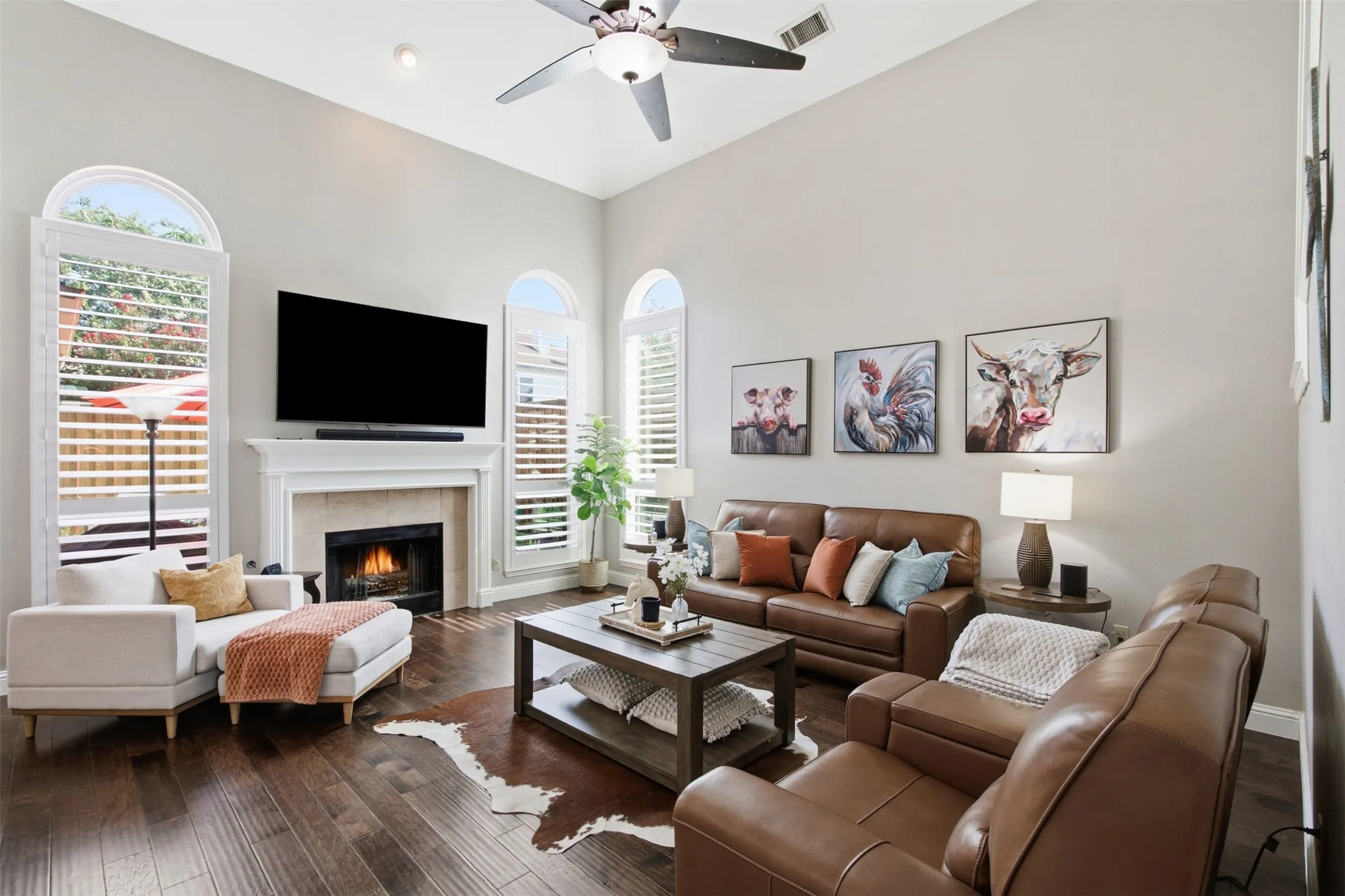 Living area featuring vaulted ceilings, wood-finish flooring, a fireplace with a white mantel, and arched windows with plantation shutters