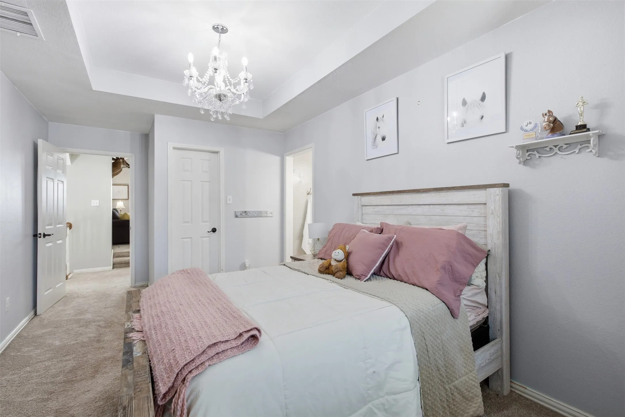 Bedroom featuring a tray ceiling with a crystal chandelier, neutral wall paint, and gray carpet flooring