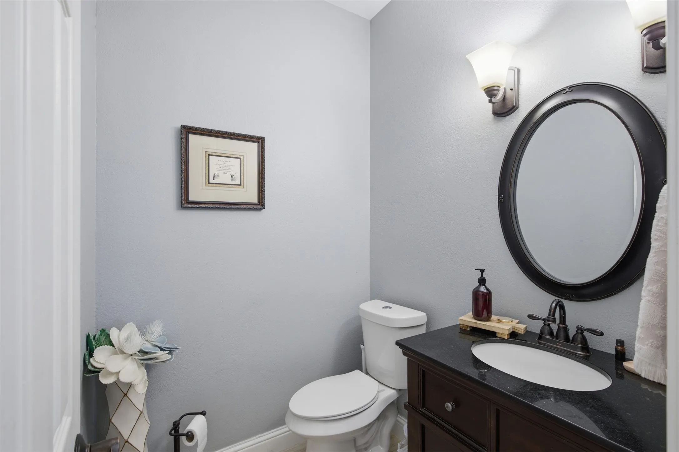 Vanity with dark wood cabinetry, a black countertop, and an oval undermount sink