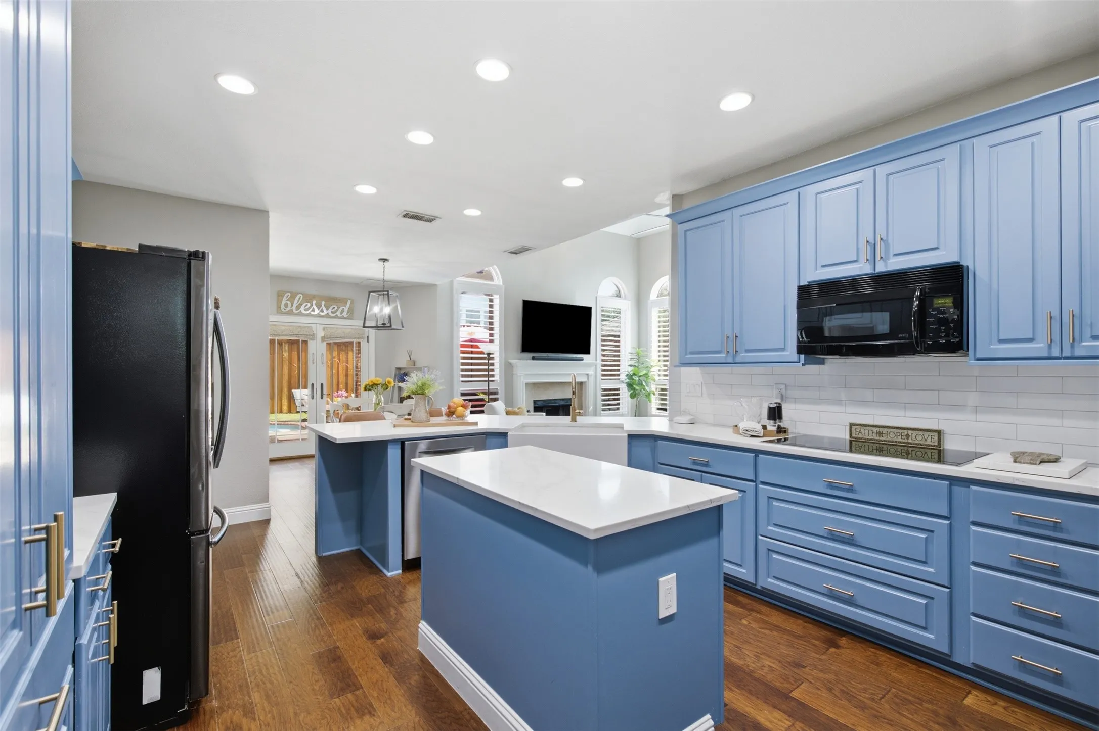 Kitchen featuring blue cabinetry, white countertops, wood-finish flooring, a built-in microwave, and a farmhouse sink