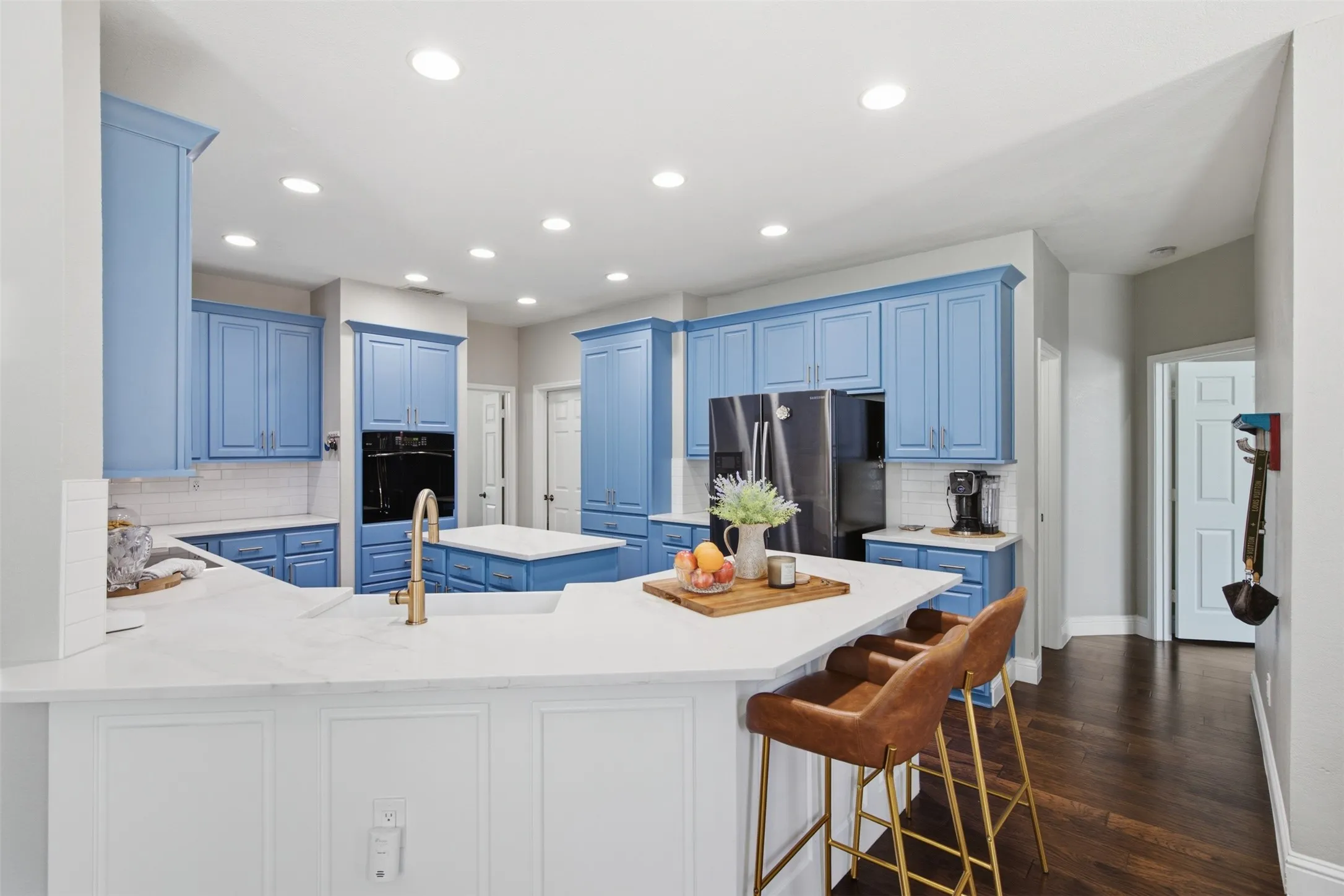 Spacious kitchen featuring perimeter blue cabinetry, white countertops, and a central island with a gold-finish faucet