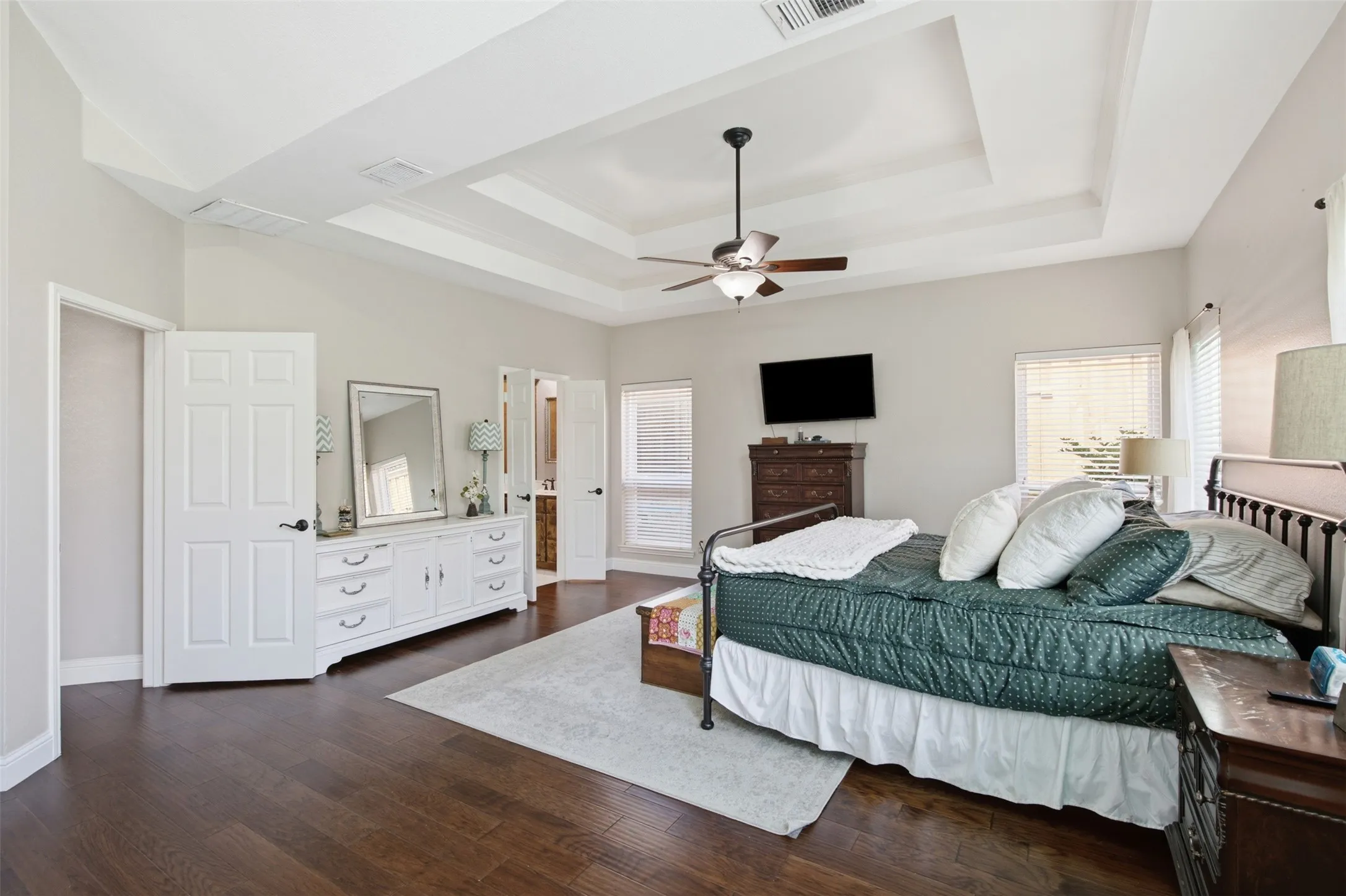 Spacious room featuring wood-finish flooring, a multi-tiered tray ceiling with a ceiling fan, and light-toned wall paint