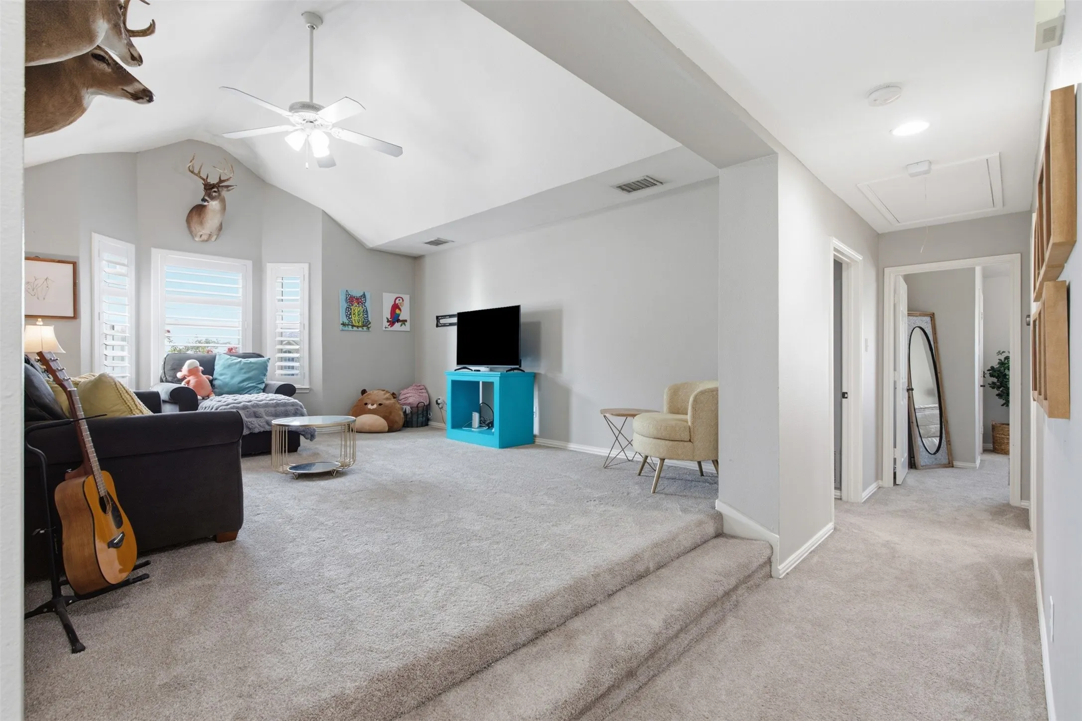 Carpeted recreation room featuring vaulted ceilings, a ceiling fan, and bay windows with plantation shutters