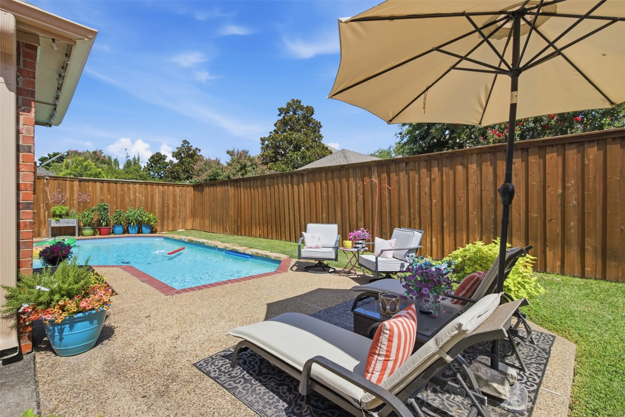 Private backyard oasis featuring a rectangular swimming pool with brick coping, a concrete patio, and a wood privacy fence
