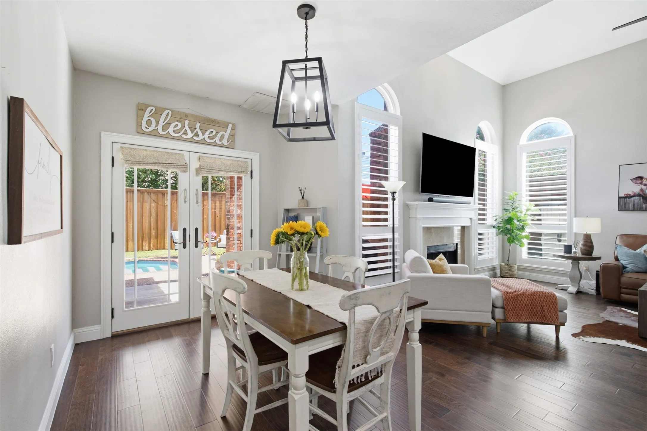 Open-concept living space featuring wood-finish flooring, a fireplace with a white mantel, and multiple arched windows with plantation shutters