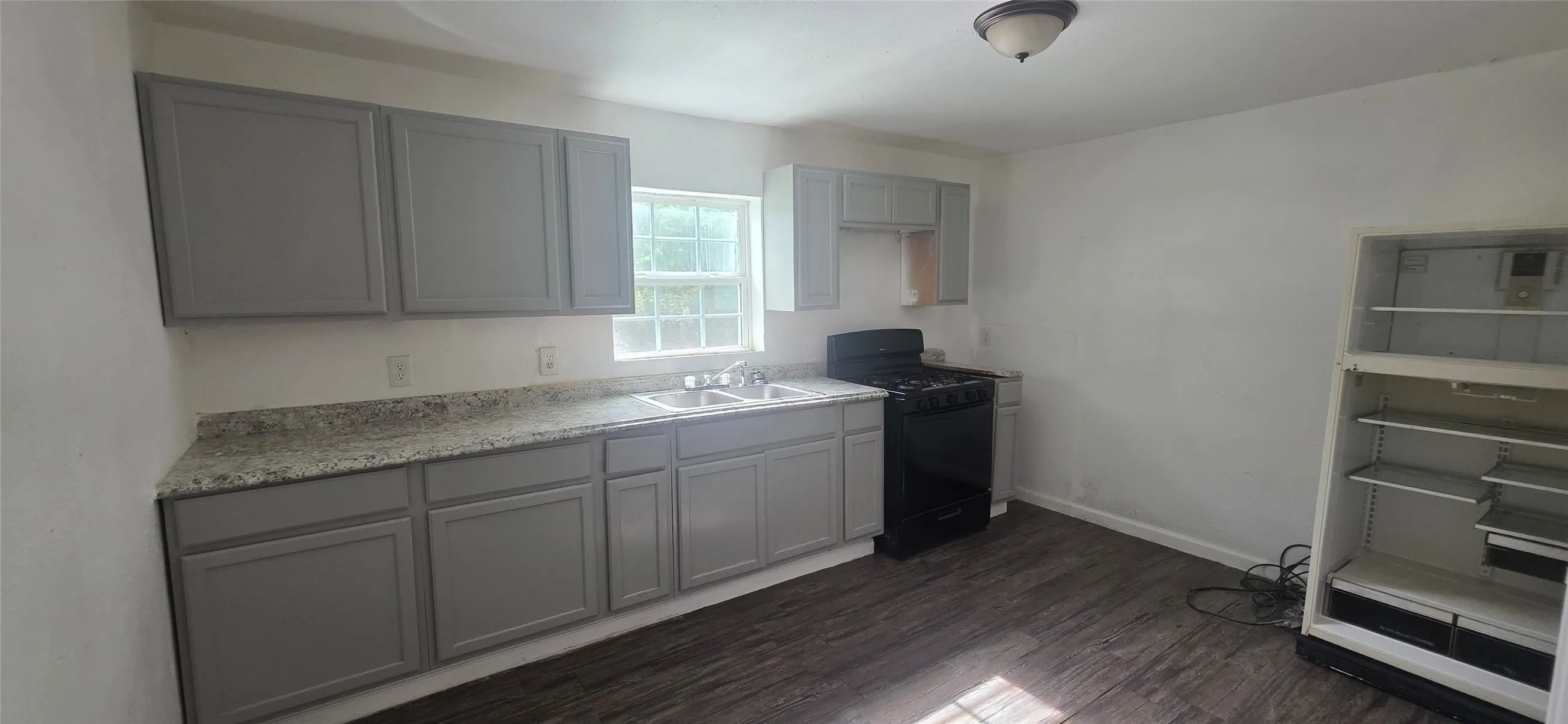 Kitchen featuring gray cabinetry, light speckled countertops, a double basin stainless steel sink, a black gas range, and dark wood-finish flooring