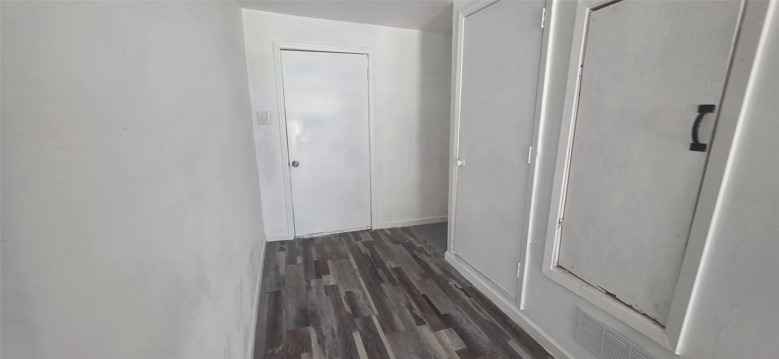 Corridor featuring wood-finish flooring, white walls, and multiple solid white doors