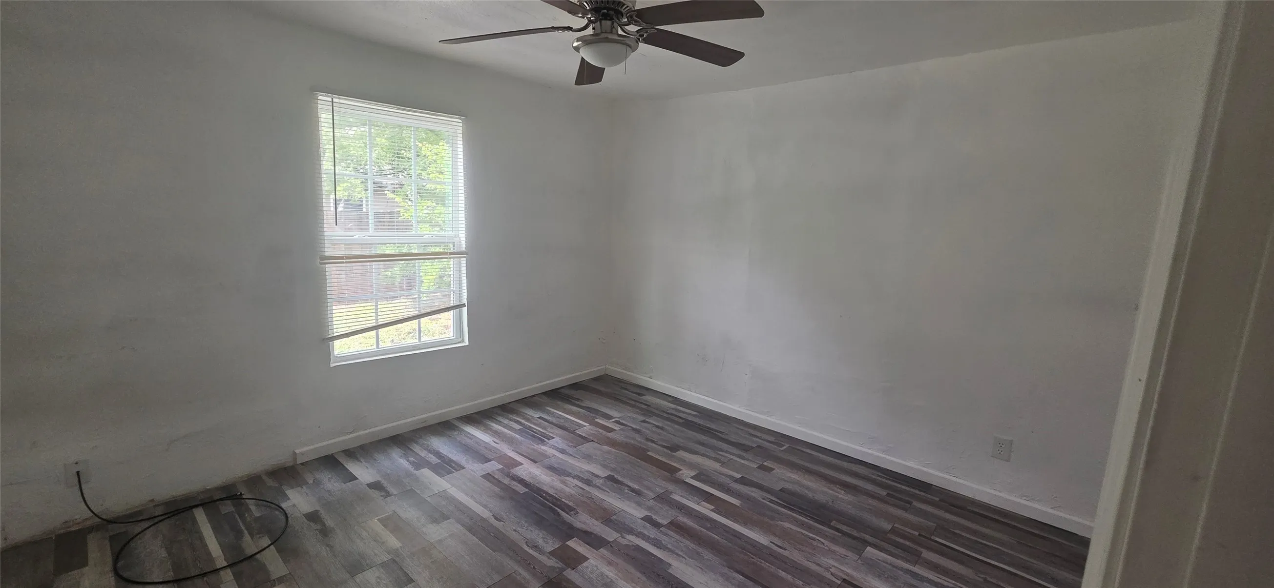 Room featuring wood-finish flooring, a window with natural light, and a ceiling fan with integrated lighting