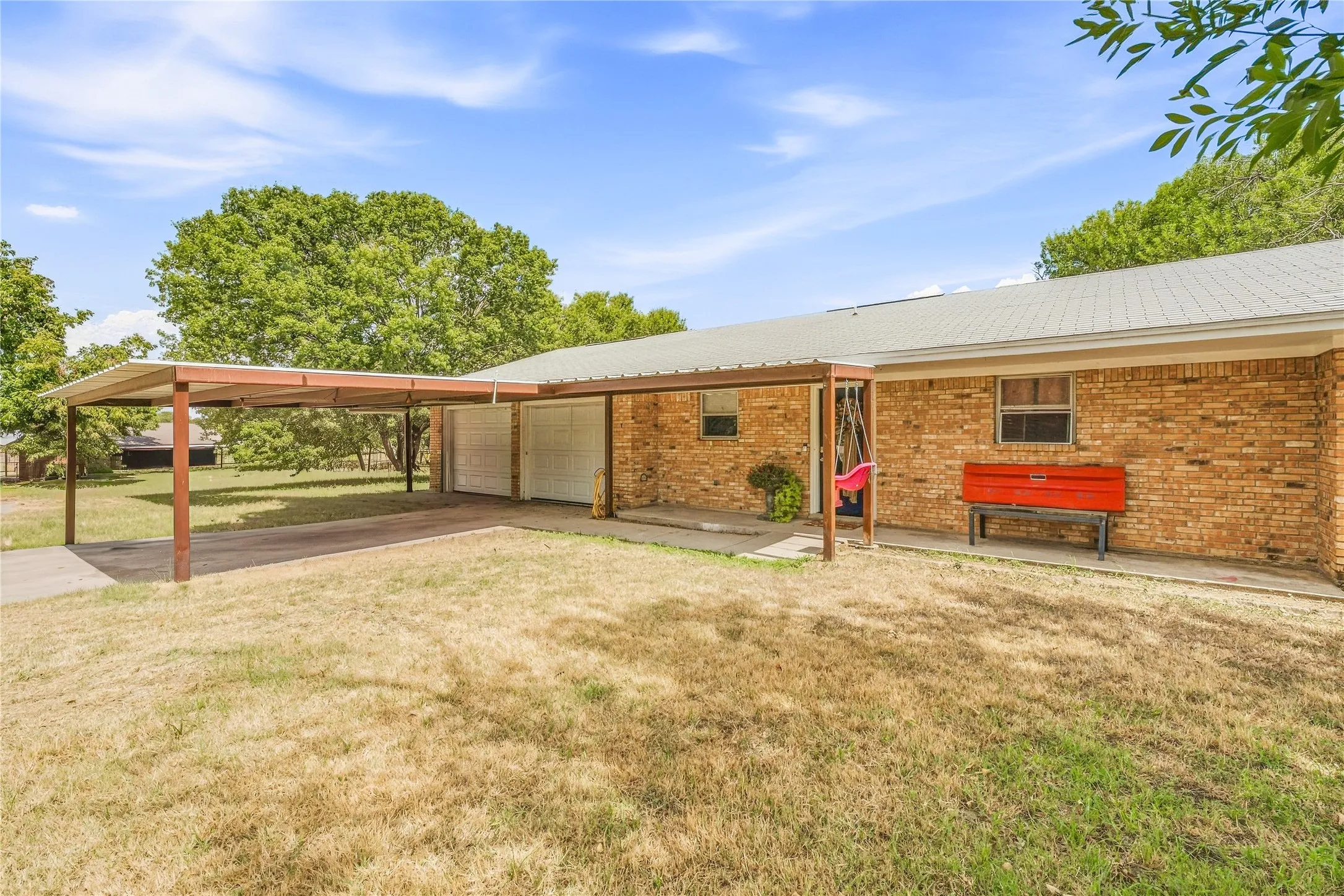 Brick exterior with a covered carport, metal roof, and paved driveway