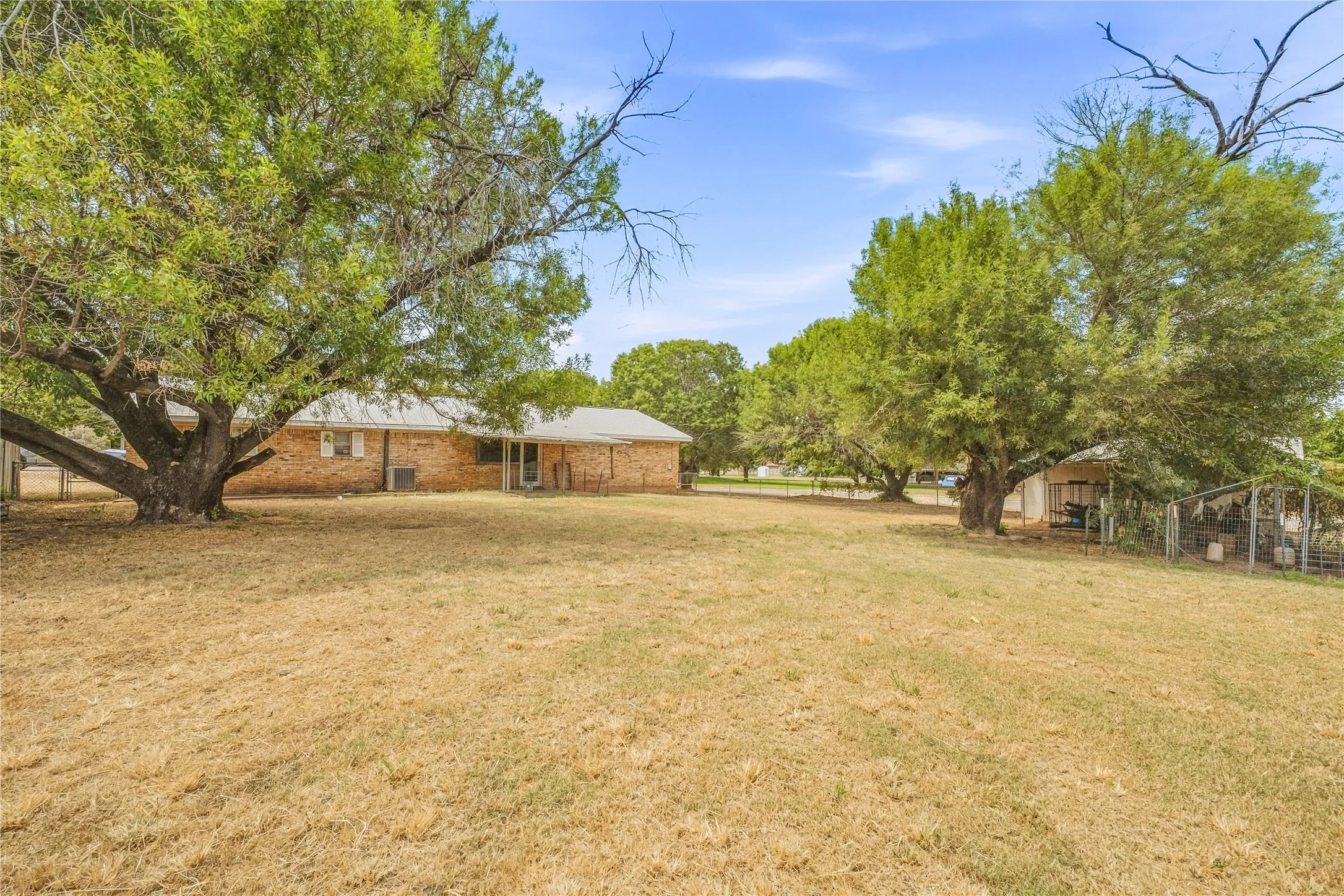 Expansive backyard with mature trees, brick exterior, and covered patio