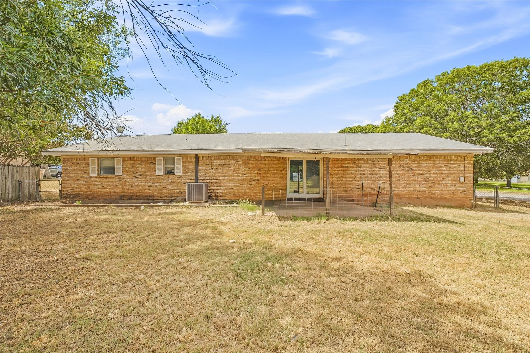 Brick exterior with multiple windows featuring shutters, an outdoor patio, and a fenced yard