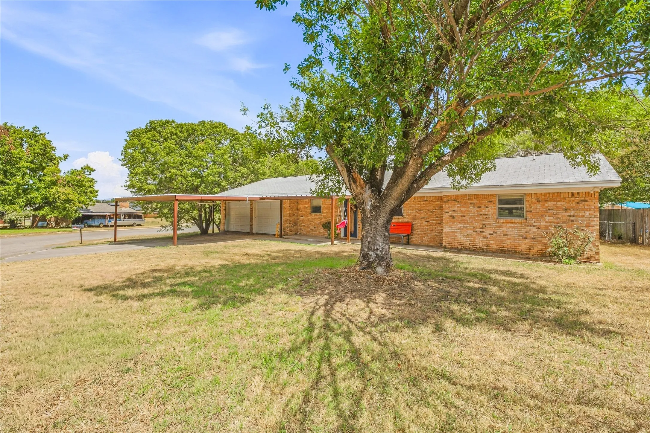 Brick exterior with metal roof, covered carport, established trees, and expansive lawn