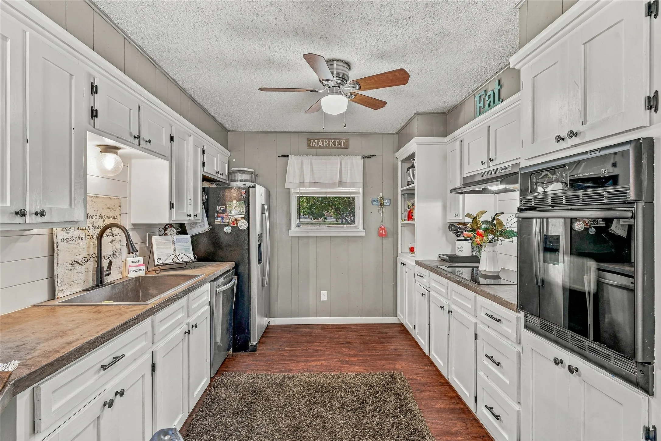 Galley kitchen featuring white cabinetry, wood-finish countertops, built-in double ovens, and wood-finish flooring