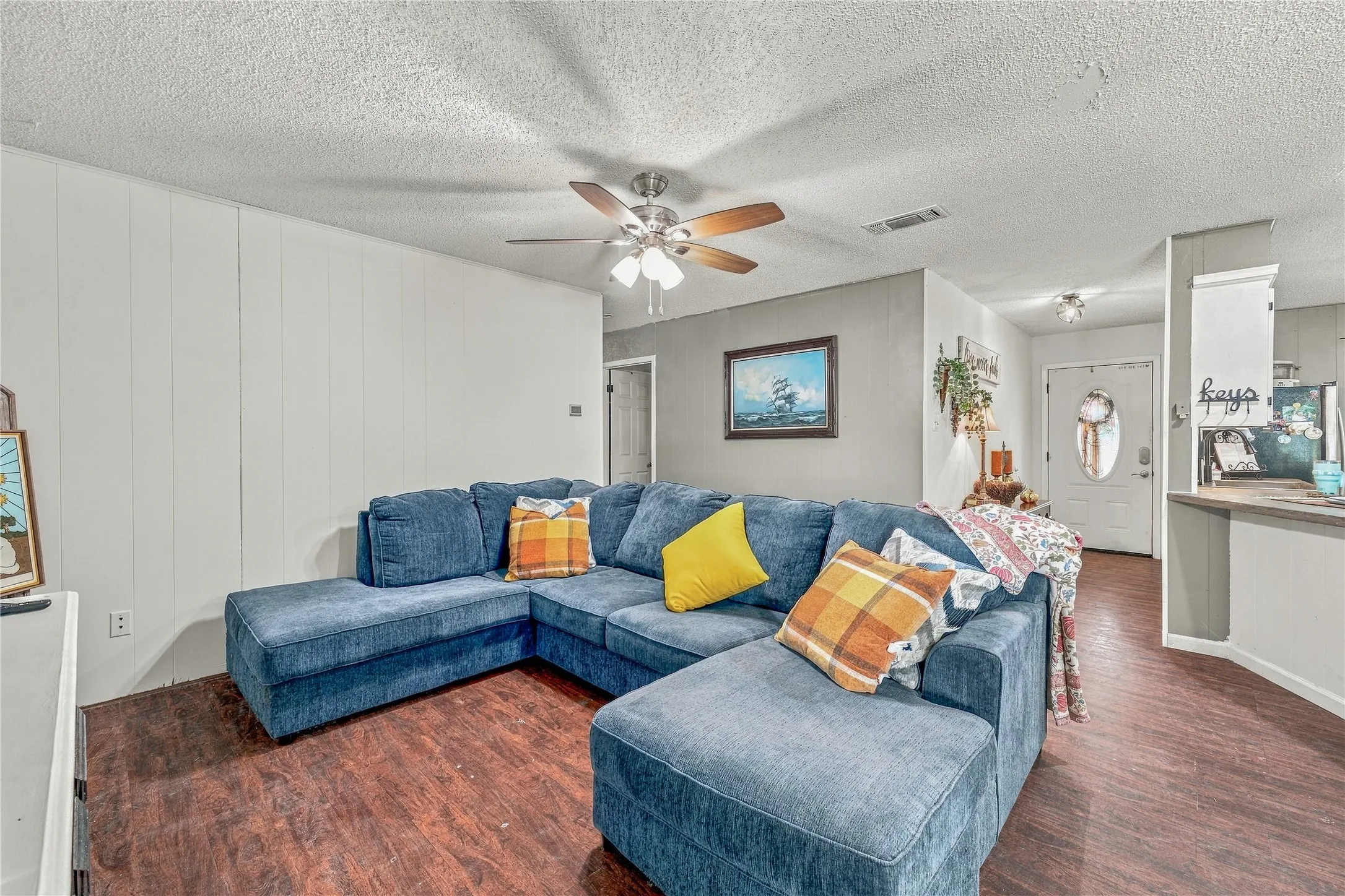 Wood-finish flooring, ceiling fan with integrated lighting, paneled accent wall, and a built-in breakfast bar