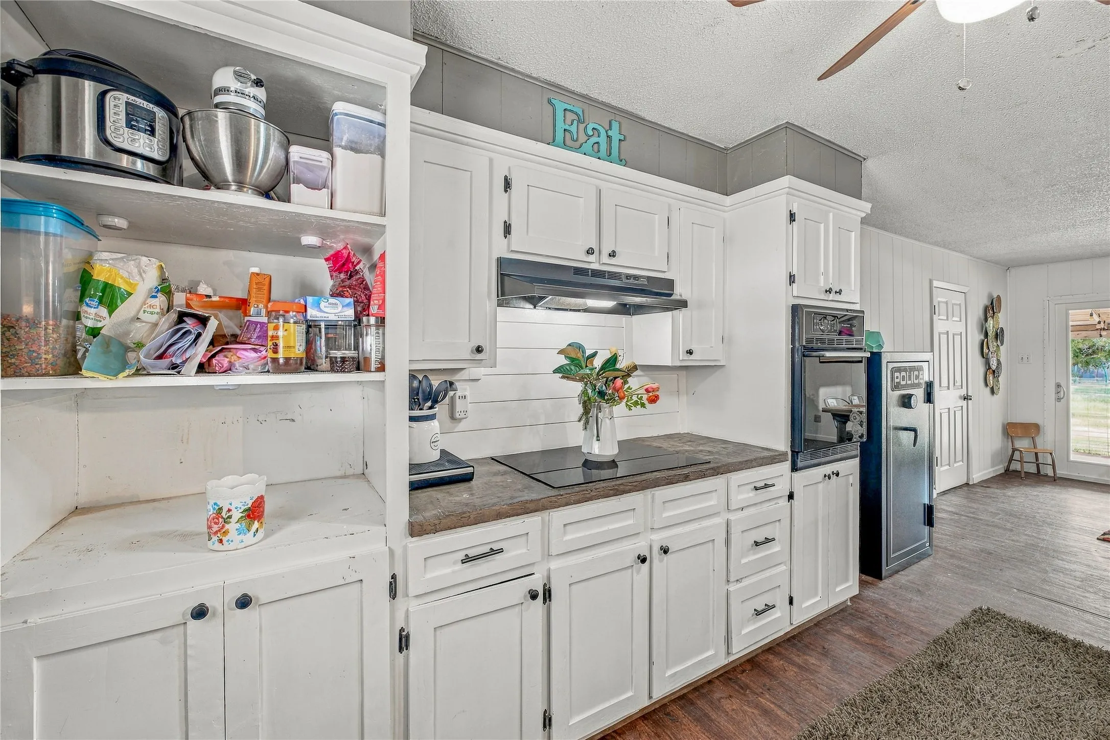 White cabinetry, built-in wall oven, dark countertop, cooktop, and wood-finish flooring