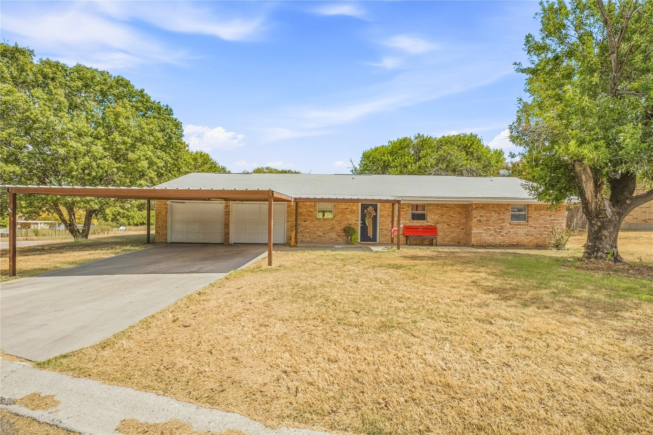 Brick exterior featuring a metal roof, extended carport, and a concrete driveway
