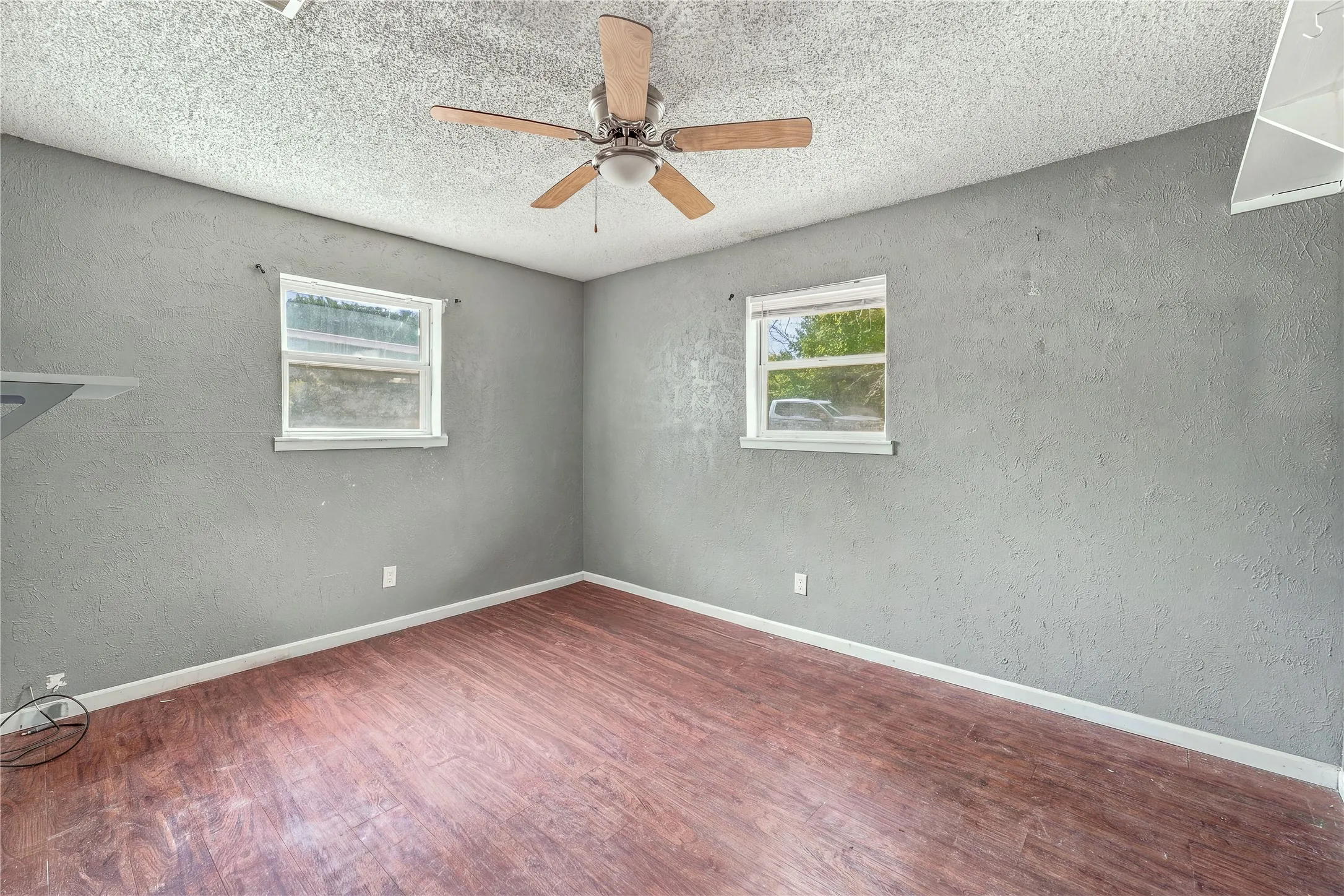 Wood-finish flooring, textured walls, and a ceiling fan with integrated lighting
