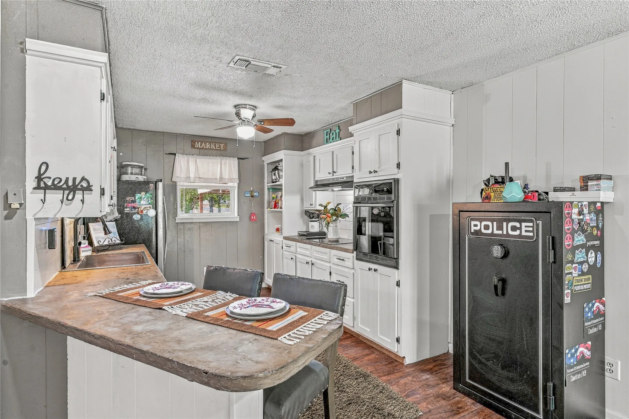 Breakfast bar with seating, white cabinetry, integrated wall oven, wood-finish flooring, and ceiling fan