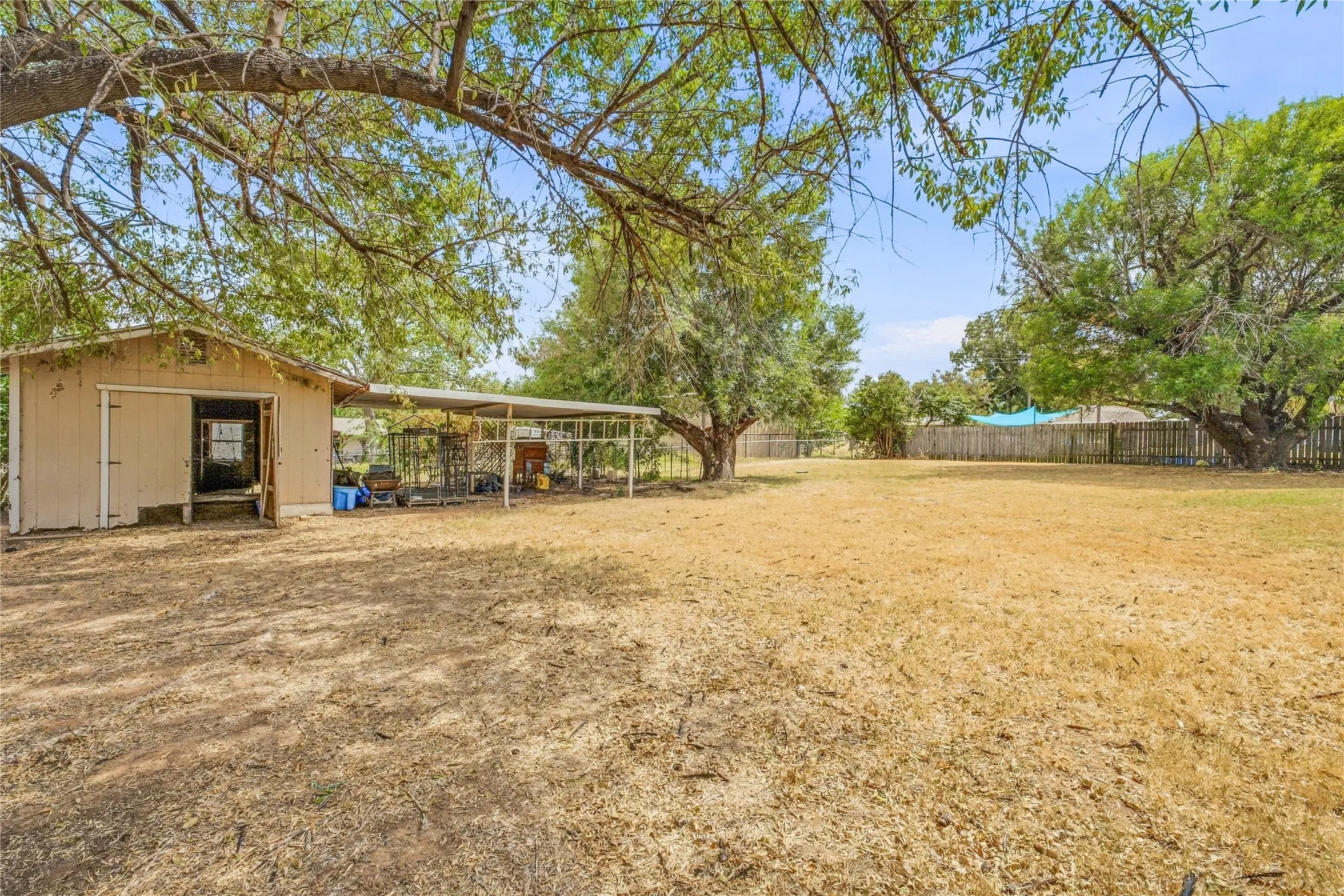 Detached outbuilding with sliding barn door, covered lean-to structure, mature trees, and wood privacy fencing
