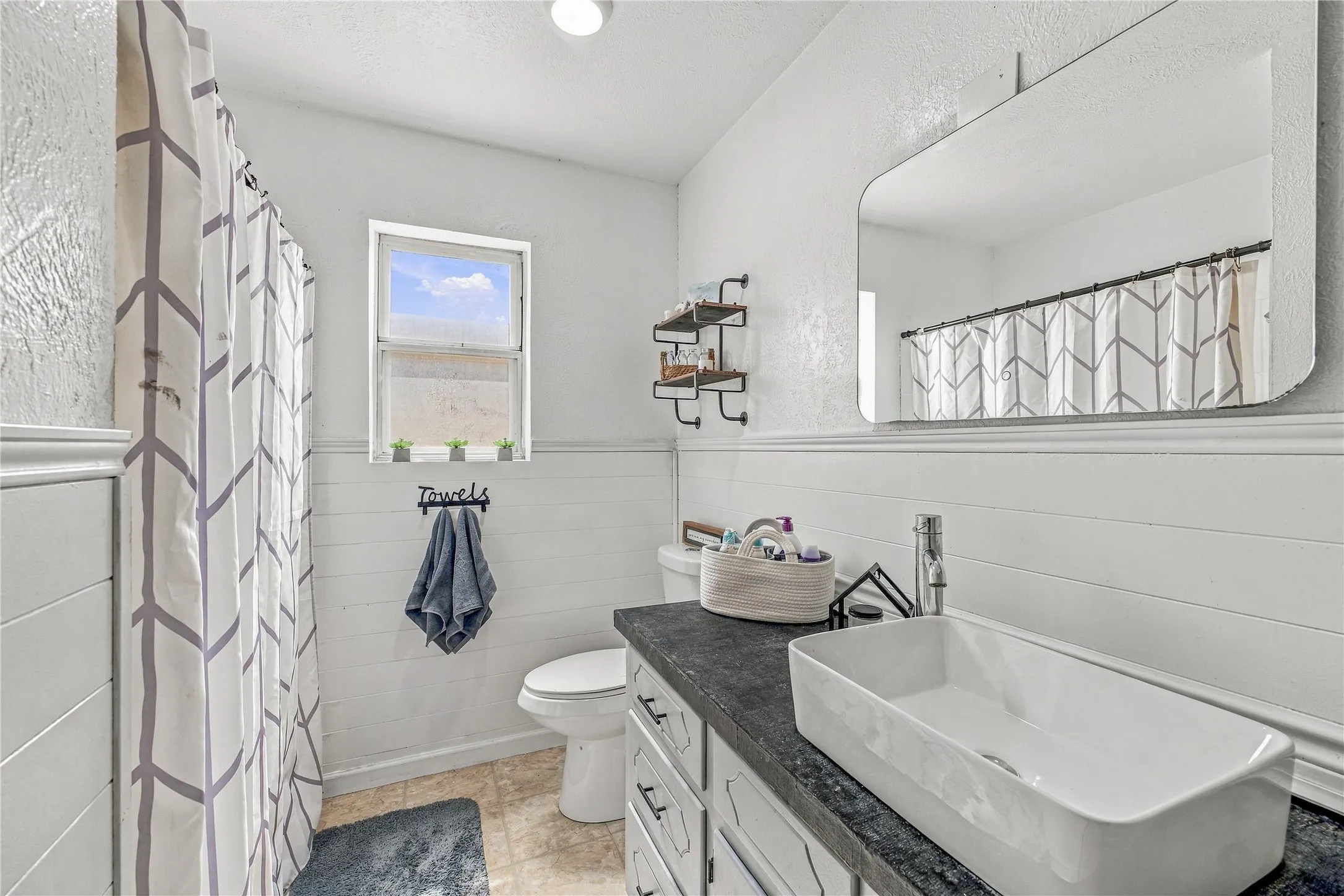 White shiplap wainscoting, rectangular vessel sink, dark countertop, and integrated shelving