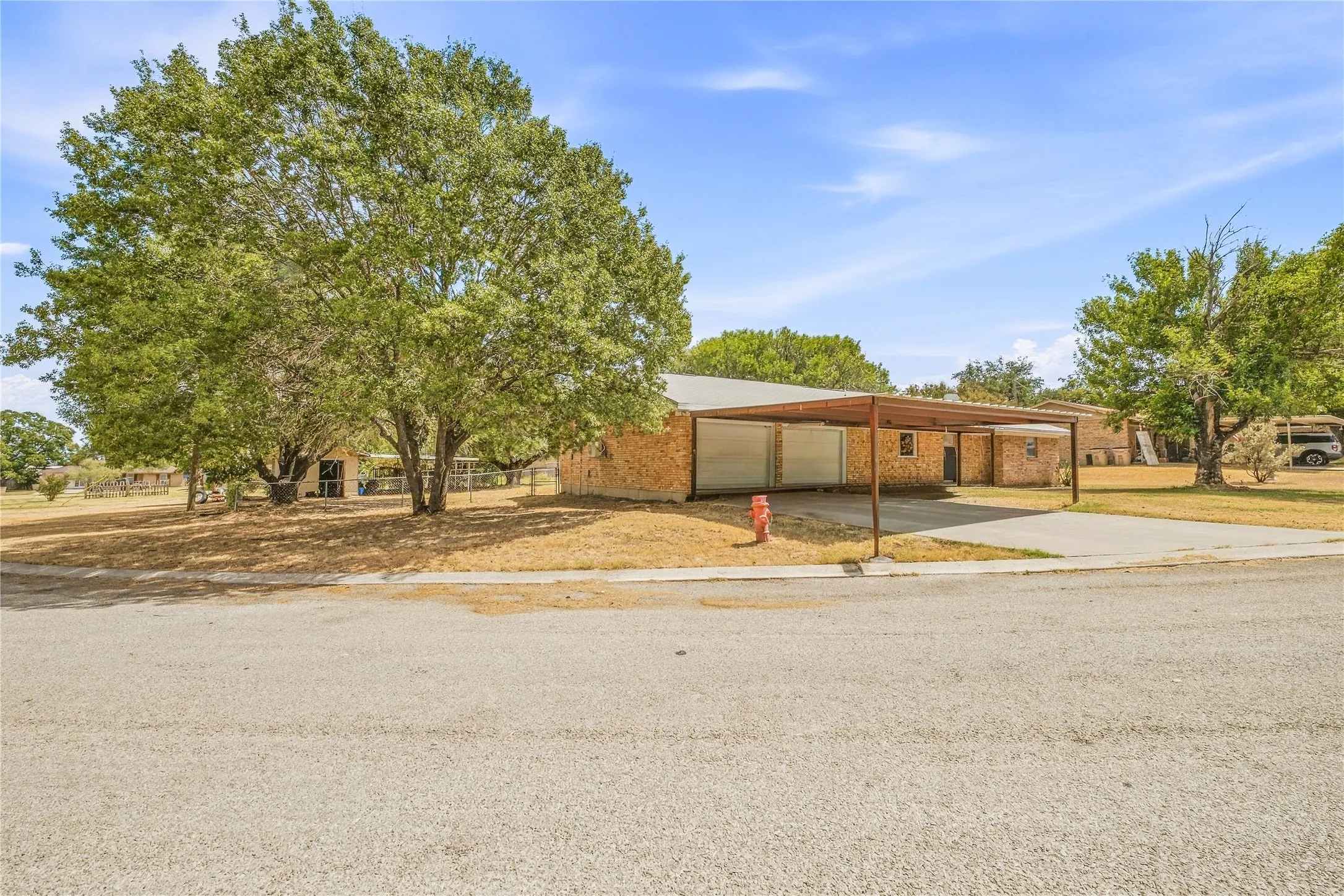 Brick exterior with a metal roof, featuring a covered carport and mature trees