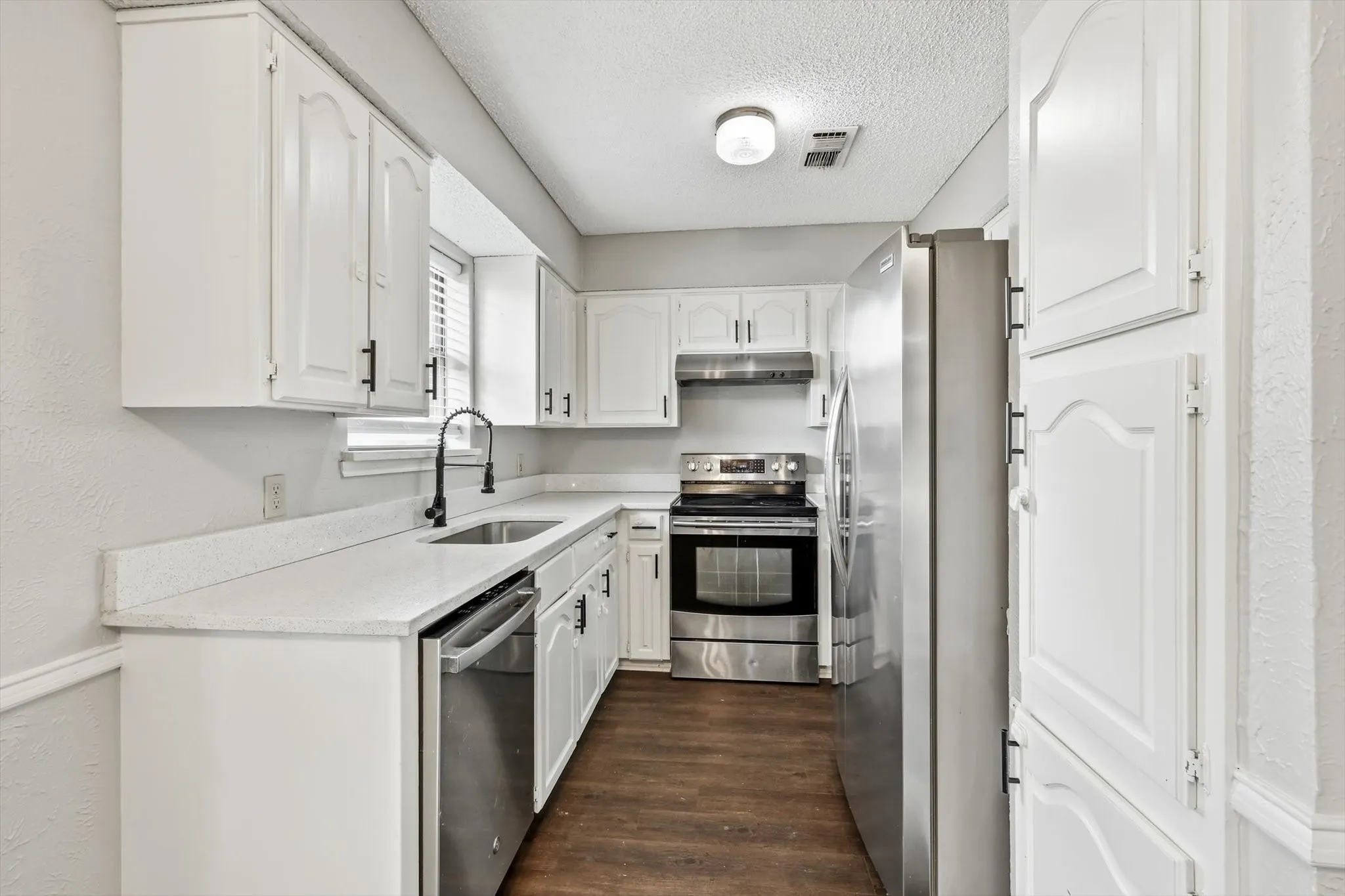 Modern kitchen featuring white cabinetry, light-toned countertops, stainless steel appliances, a black gooseneck faucet, and wood-finish flooring