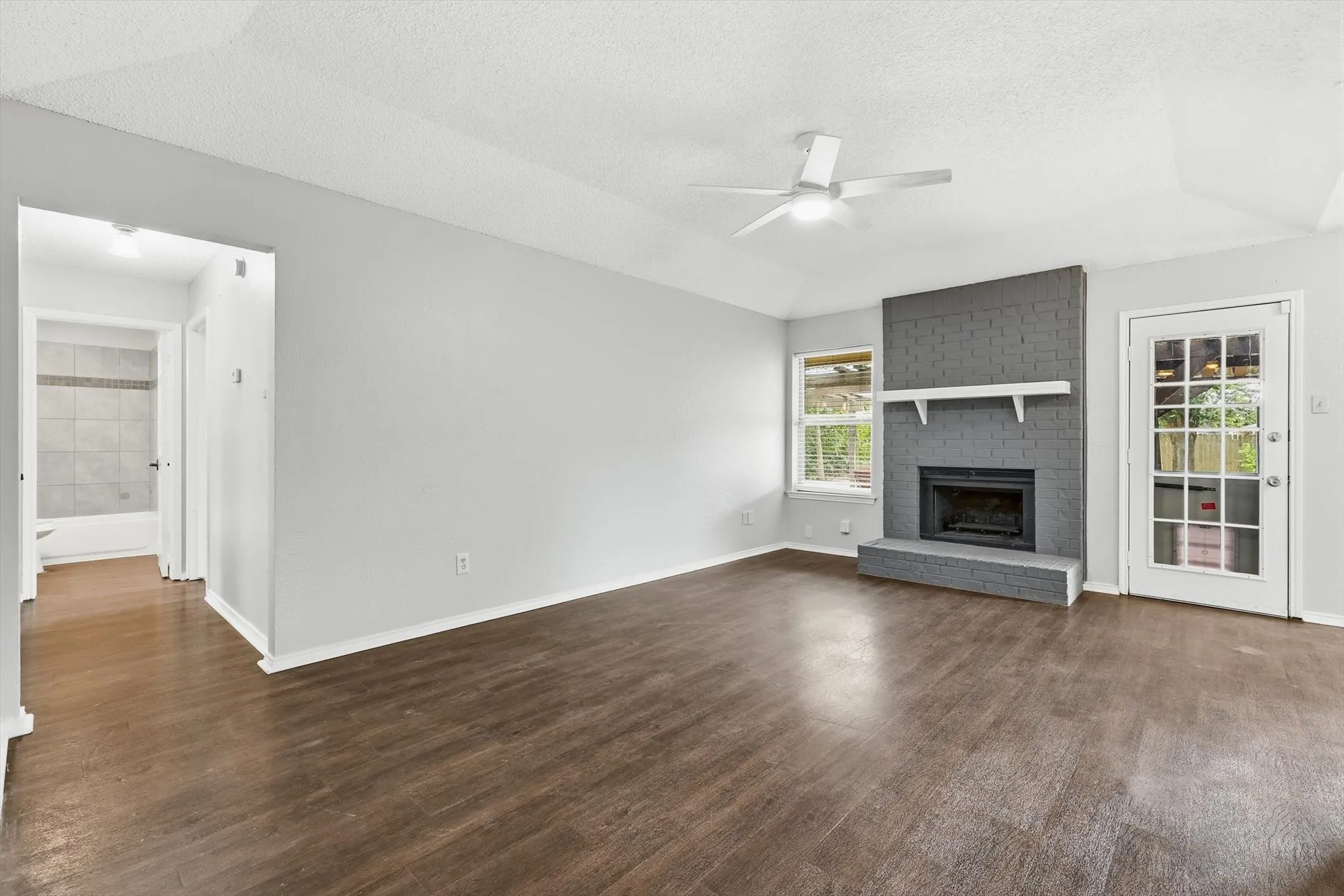 Living area featuring wood-finish flooring, a painted brick fireplace with a white mantel, and a ceiling fan