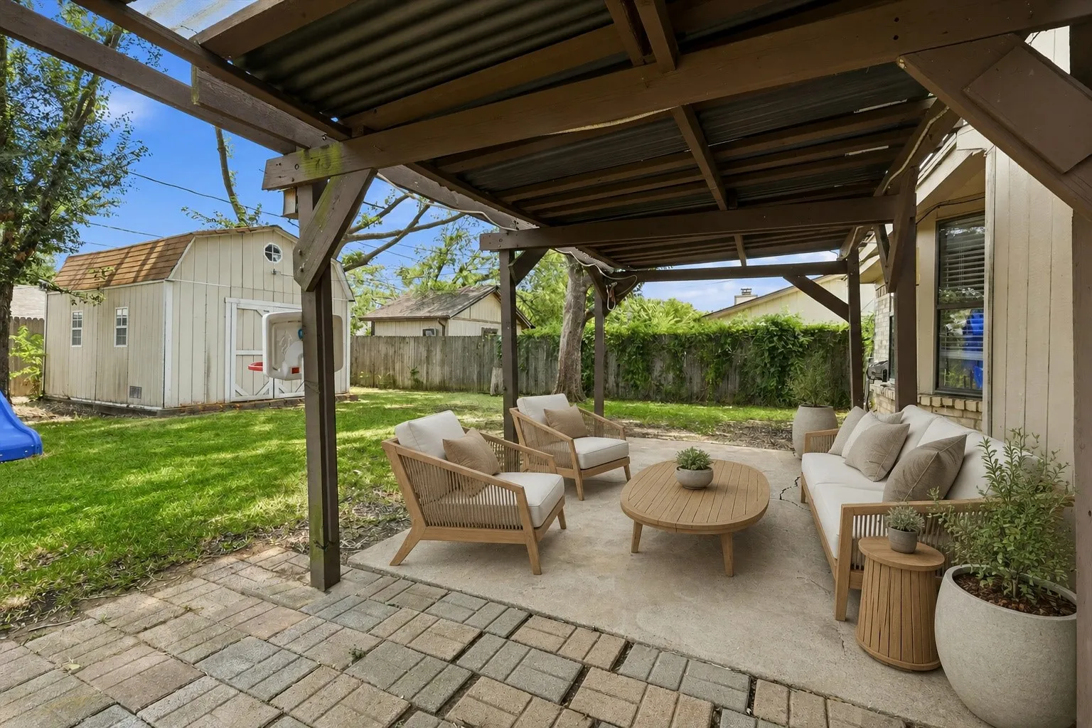 Virtually Staged Covered patio with wood-beam pergola and paver foundation overlooking manicured lawn and mature landscaping
