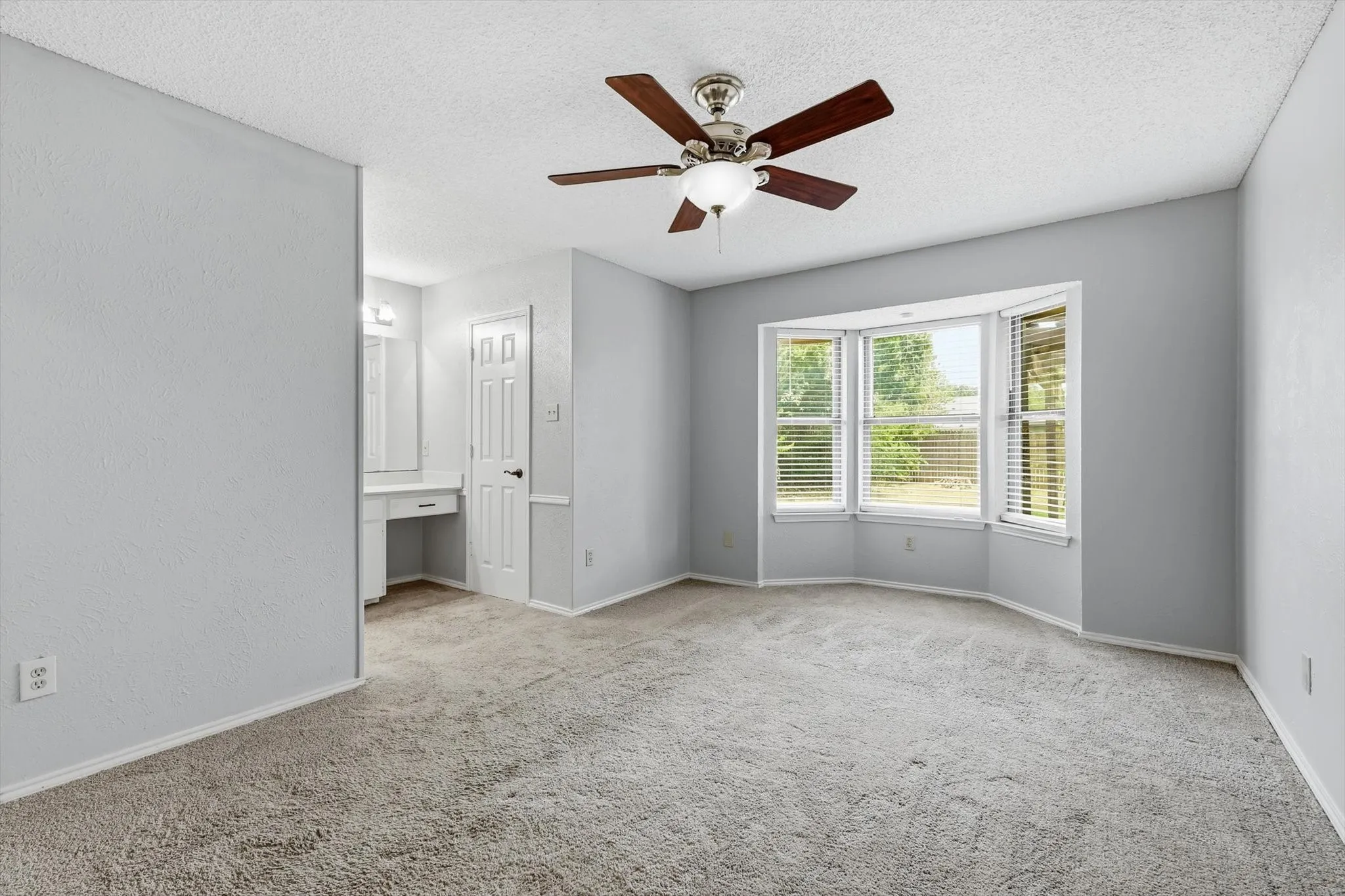 Spacious room with a bay window, ceiling fan, and carpet flooring
