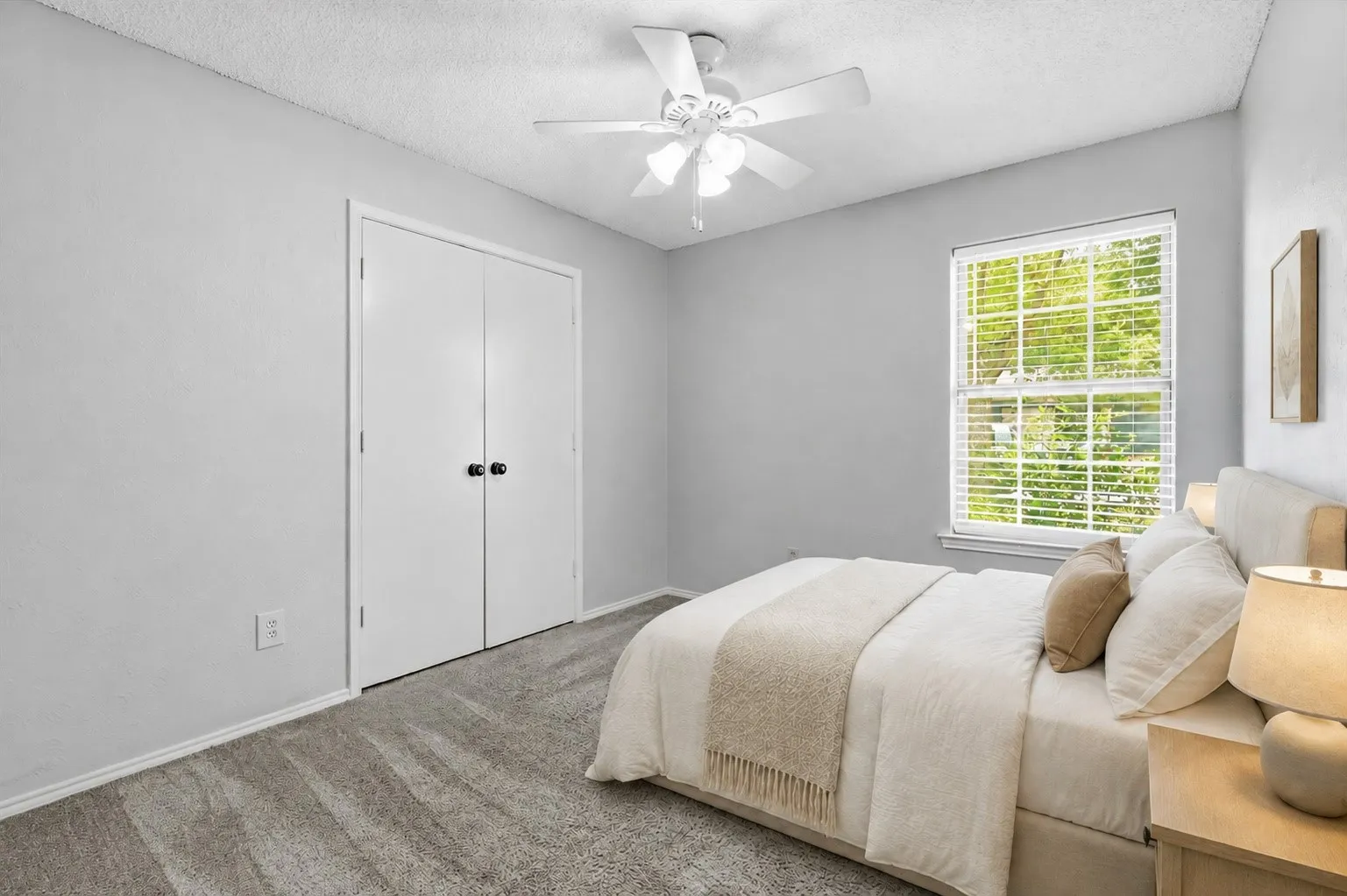 Virtually Staged Room with neutral gray walls, textured carpeting, a double-door closet with black hardware, a window with horizontal blinds, and a white ceiling fan with integrated lighting