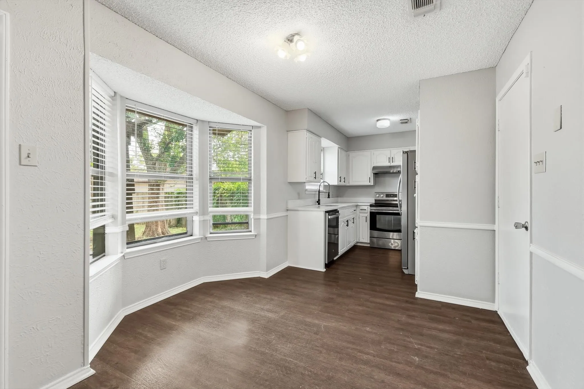 Bright kitchen featuring white cabinetry, stainless steel appliances, and a wood-finish plank floor