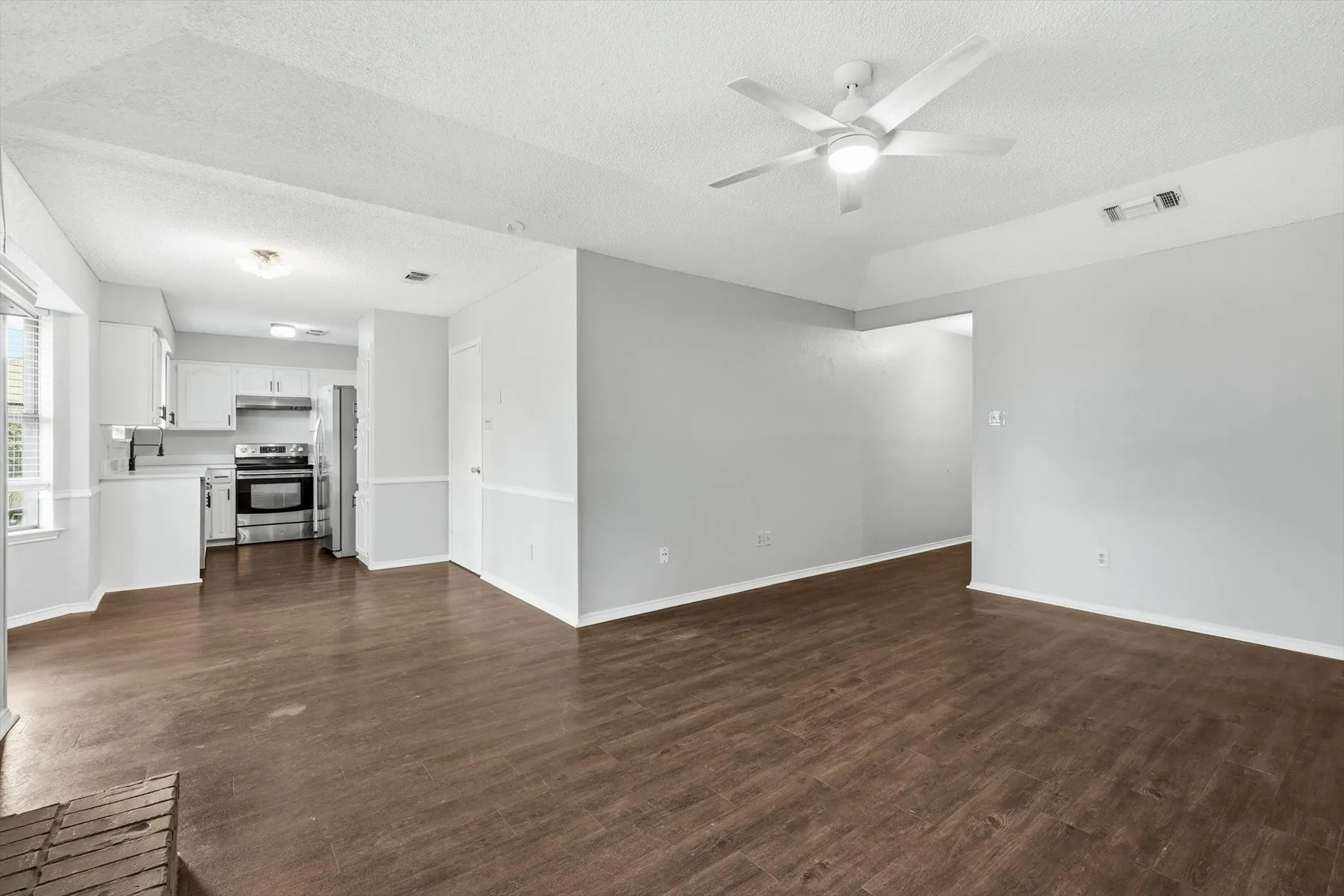 Open concept living area featuring wood-finish flooring, light grey walls, and a white ceiling fan with integrated lighting