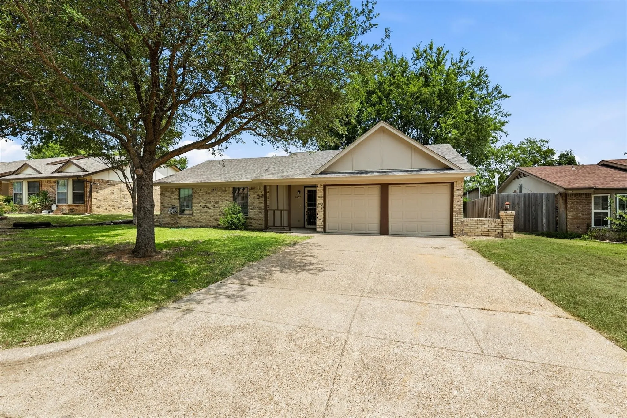 Brick facade residence featuring a two-car garage, concrete driveway, and mature front yard tree