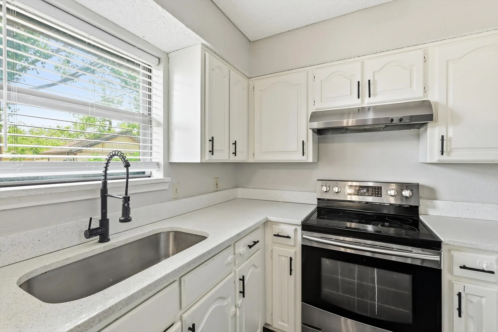 Kitchen featuring white cabinetry with black hardware, white countertops, a stainless steel sink with a black pull-down faucet, a stainless steel range with a black cooktop, and a matching stainless steel range hood